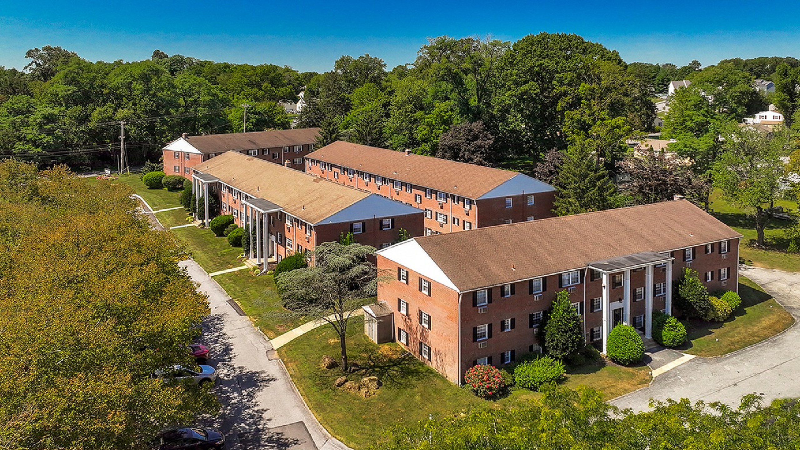 Charming brick apartment complex nestled in lush greenery, showcasing classic architectural design and a serene suburban setting.