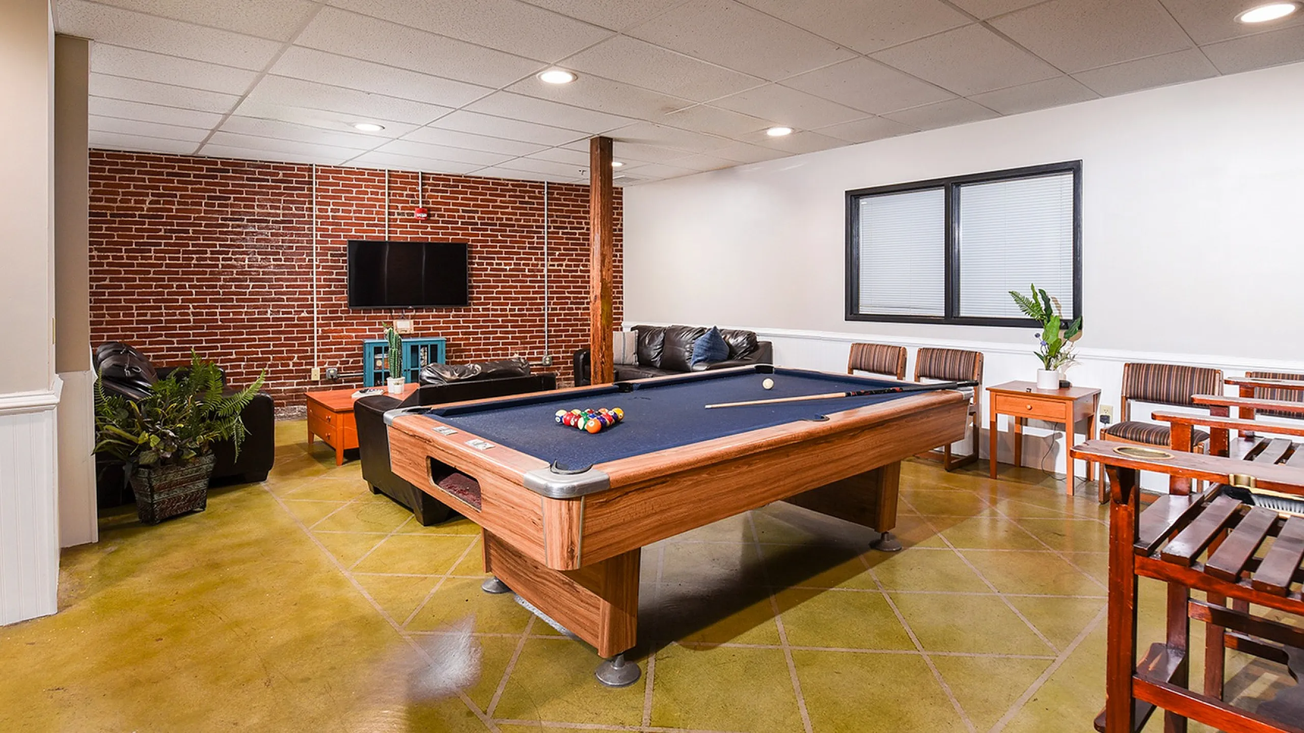 Chic recreation room with a pool table, cozy seating area, and vibrant brick accent wall, perfect for entertaining.