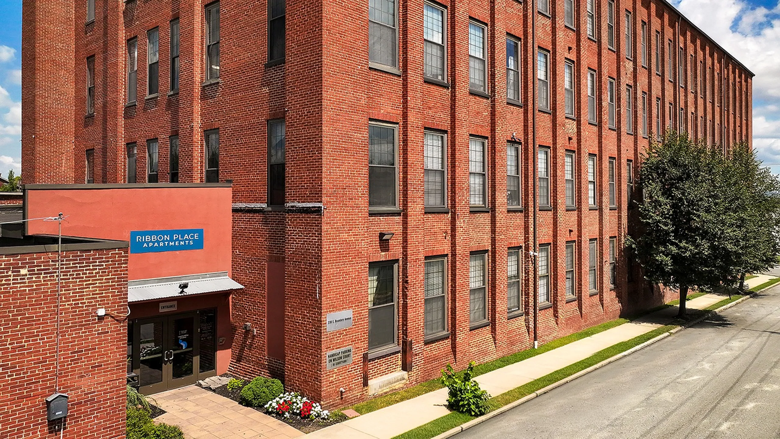 Charming brick exterior of Ribbon Place Apartments with lush landscaping, showcasing a blend of historic architecture and modern living.