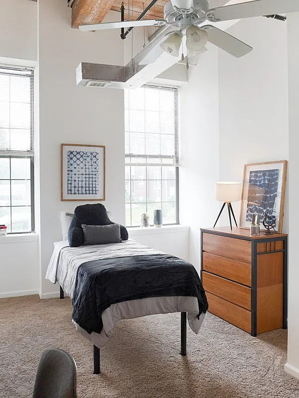 Bright, modern bedroom with cozy twin bed, stylish wooden dresser, and large windows showcasing abundant natural light, perfect for a serene retreat.