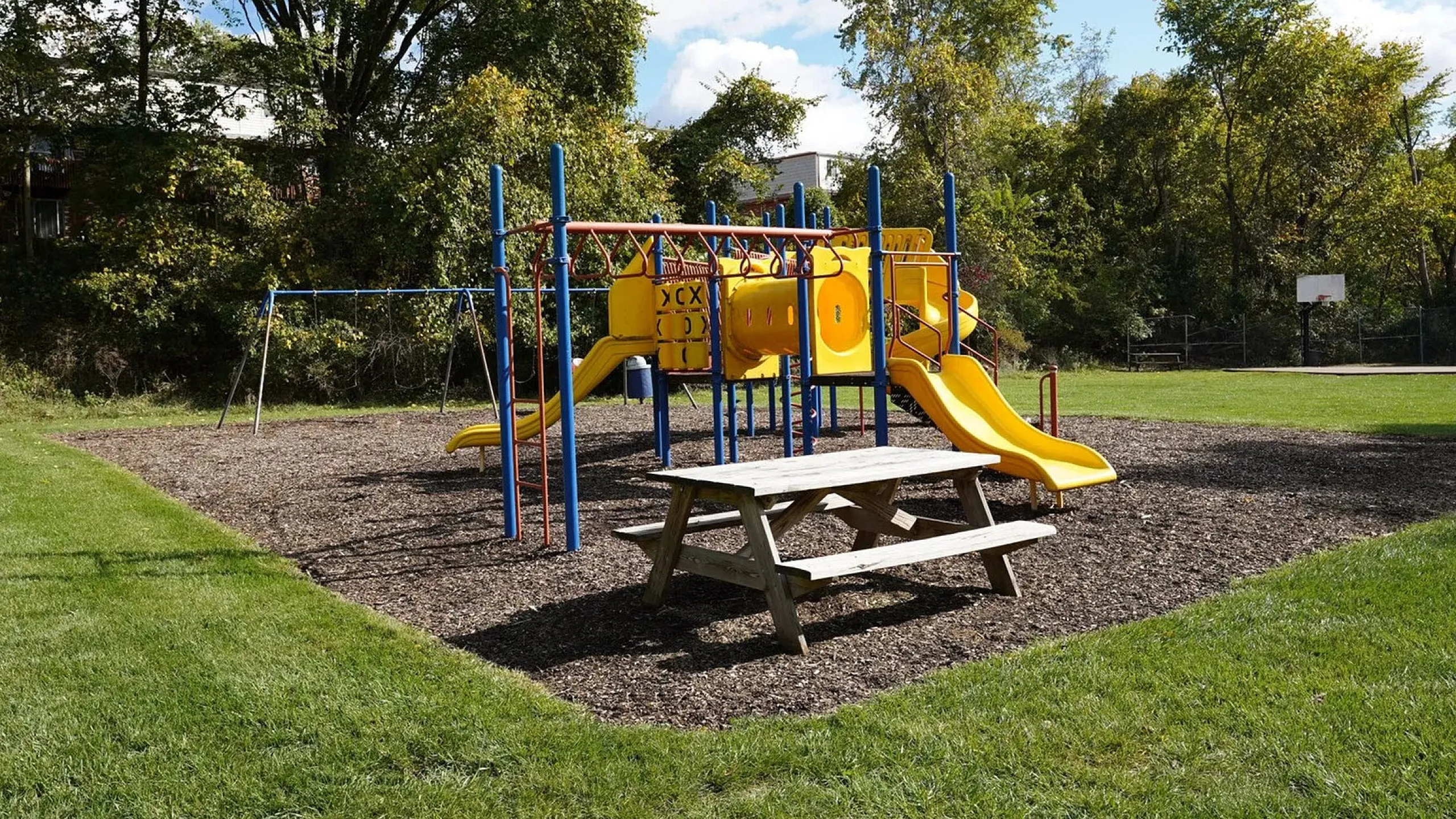 Inviting playground with vibrant yellow slides, swing set, and picnic table set amidst lush greenery, ideal for family enjoyment.