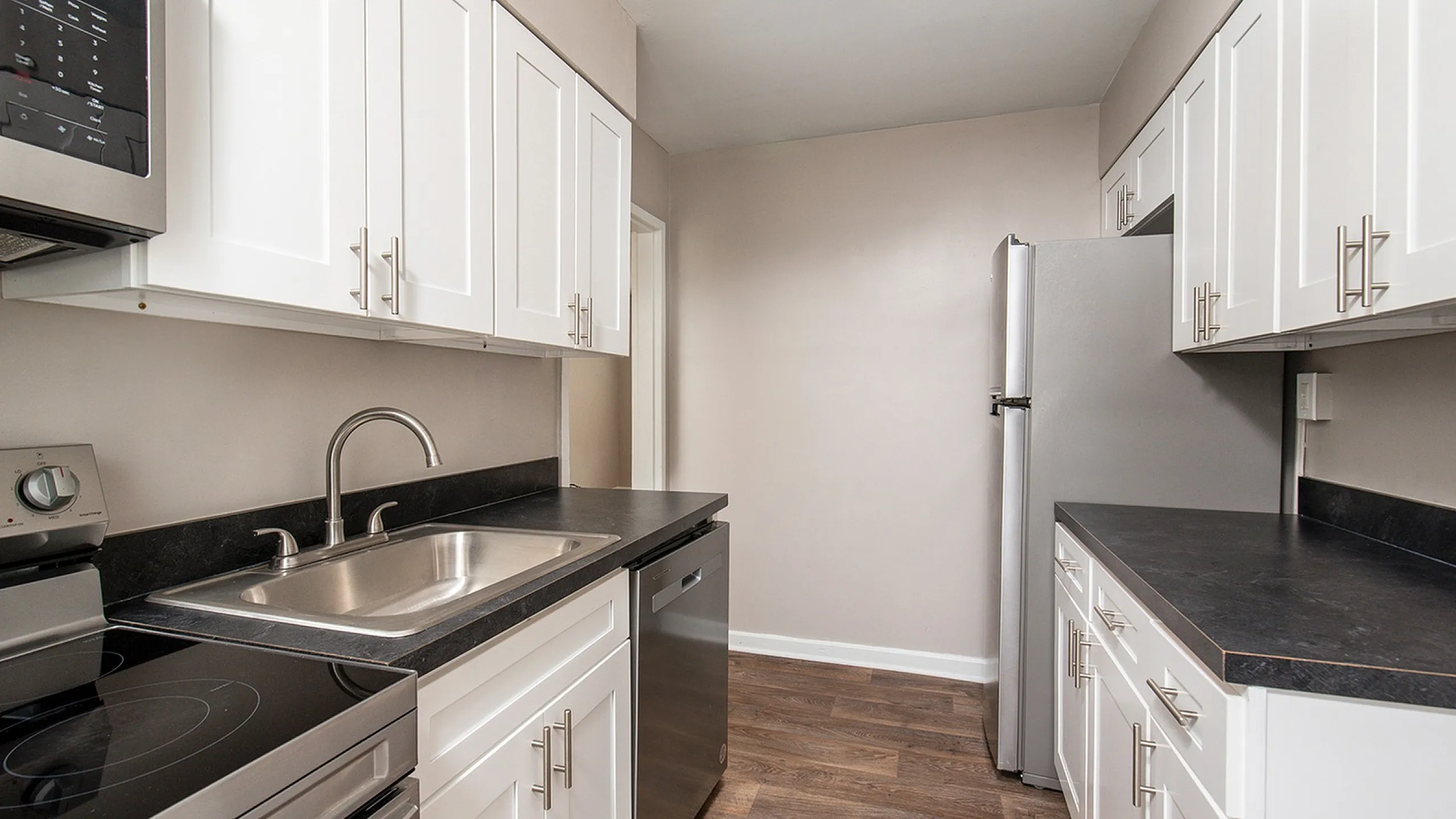 Modern kitchen with sleek stainless steel appliances, elegant white cabinetry, and a stylish black countertop. Warm wood flooring adds charm and sophistication.