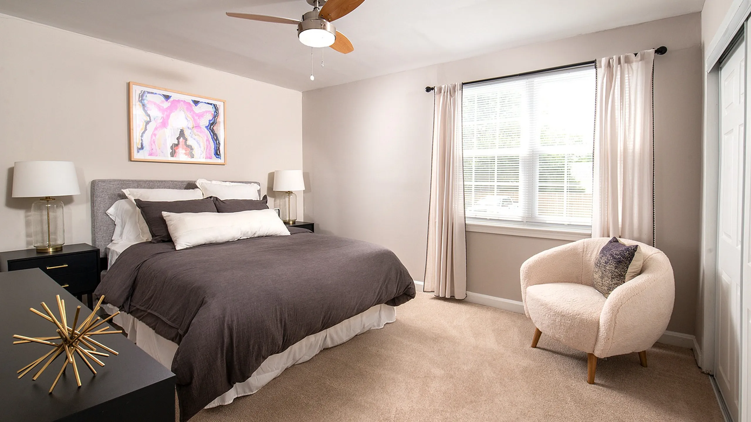 Elegant bedroom featuring a plush bed with gray bedding, stylish decor, and ample natural light through a large window.