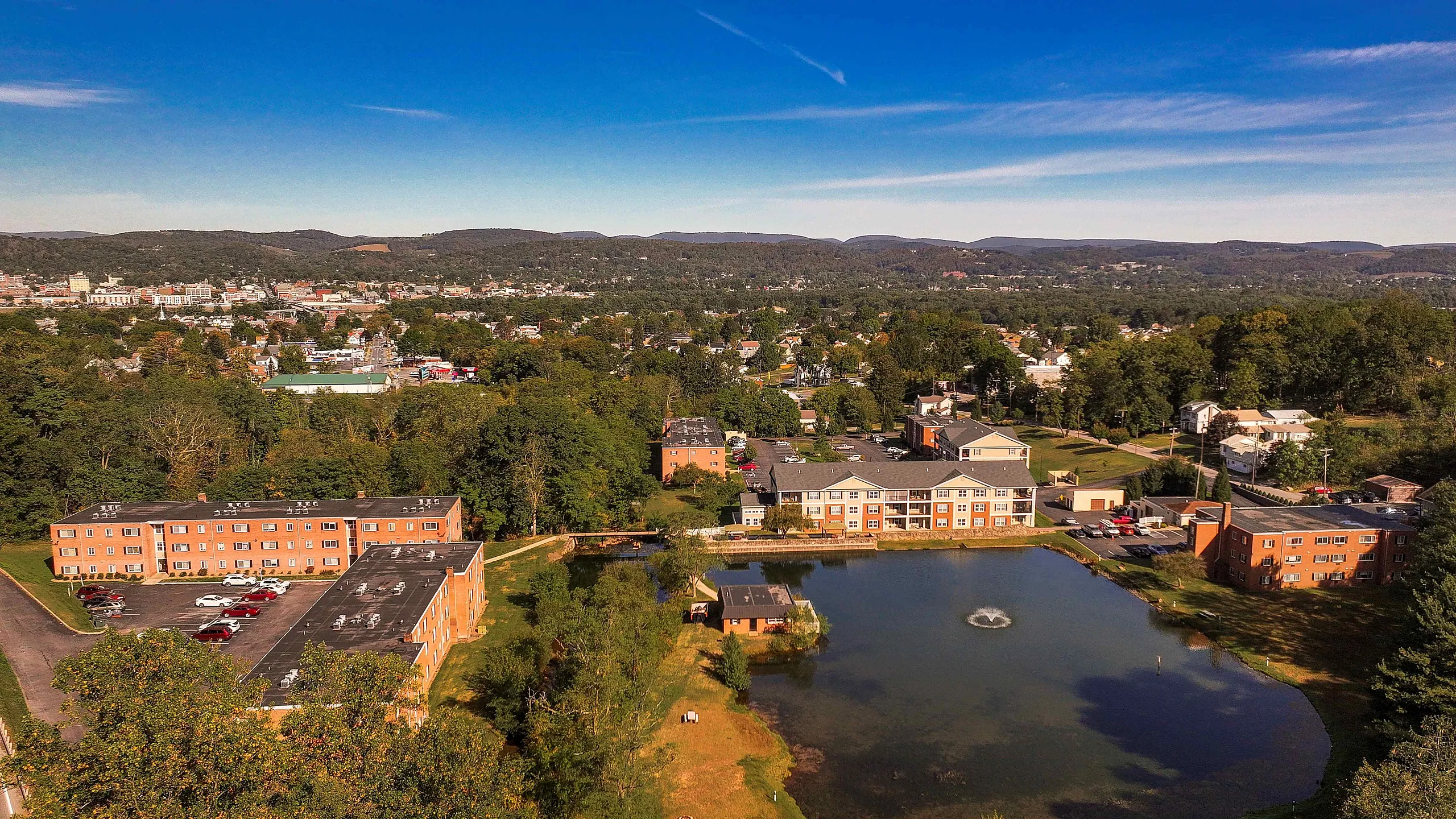 Breathtaking aerial view of a serene apartment complex surrounded by lush greenery and a tranquil pond, offering a perfect blend of nature and urban living.