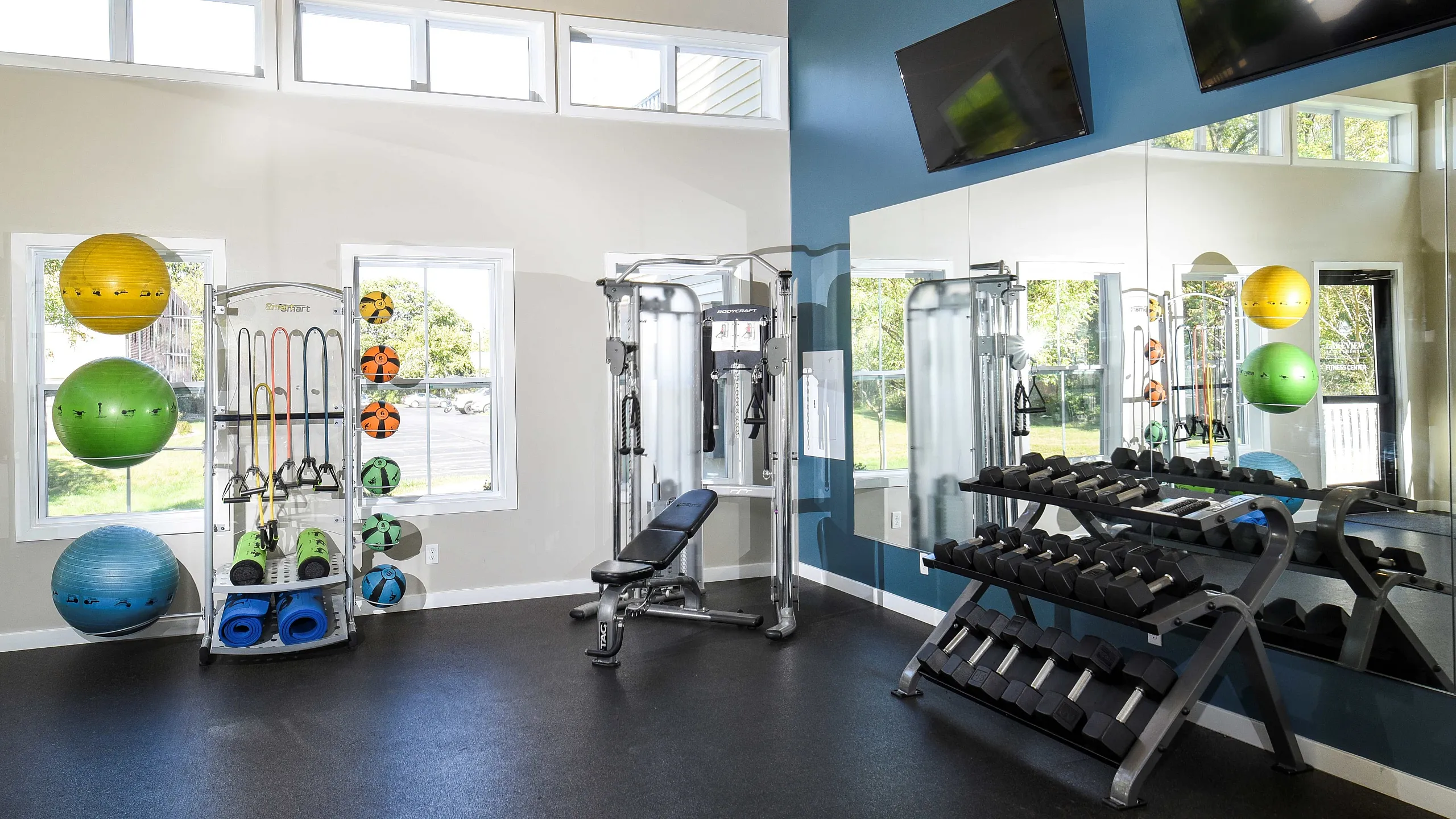 Modern fitness center with bright windows, weight racks, exercise balls, and versatile gym equipment, ideal for an invigorating workout.