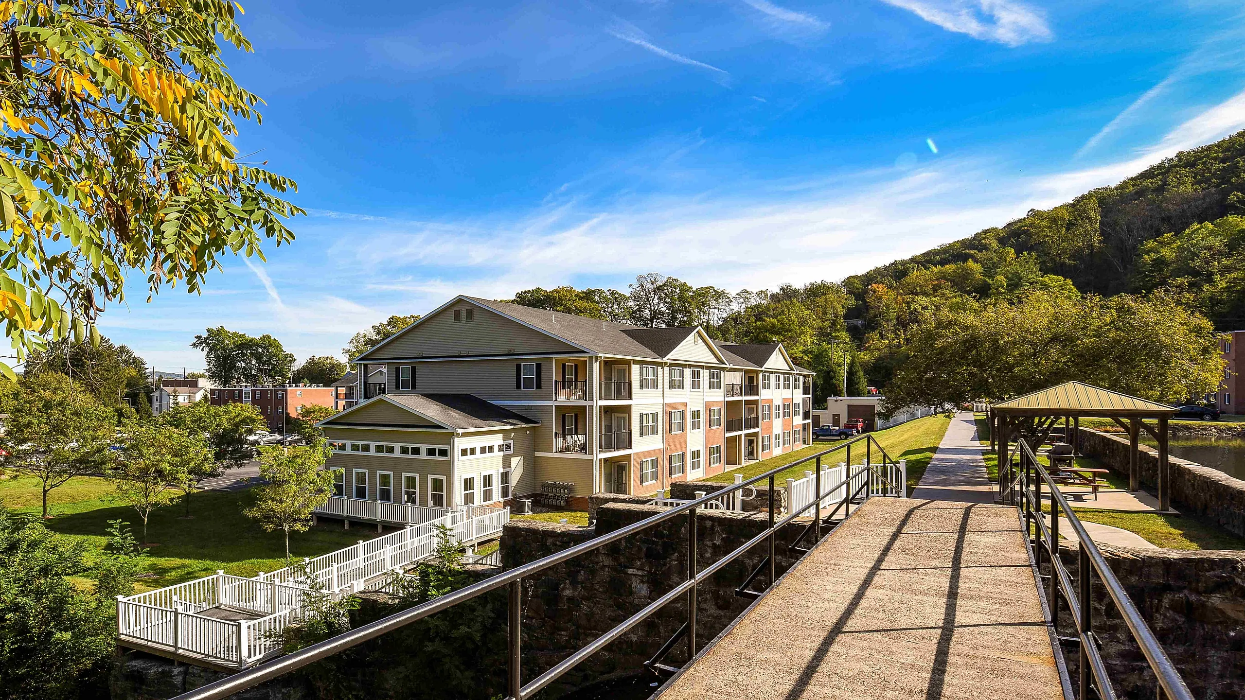 Charming apartment building surrounded by lush greenery and picturesque trails under a bright blue sky.