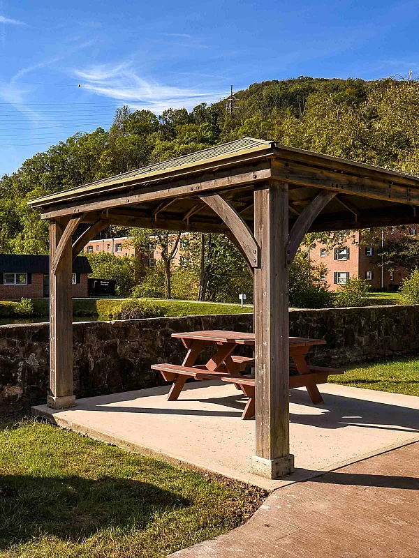 Charming outdoor gazebo with a picnic table and grill by a serene lake, surrounded by lush greenery and scenic views.