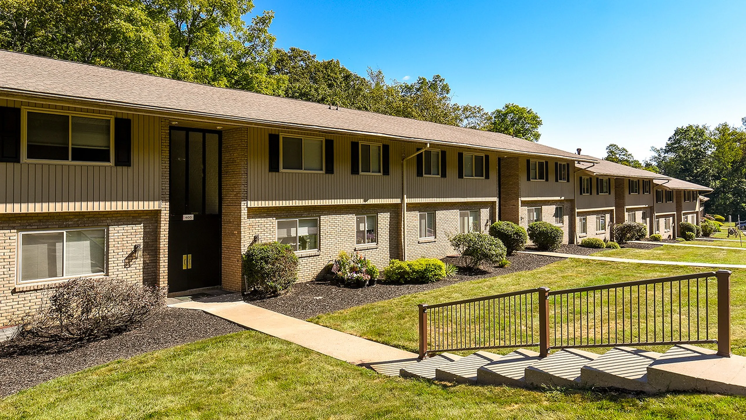 Charming row of brick apartments nestled in a lush, green landscape, highlighted by abundant sunlight and manicured lawns.