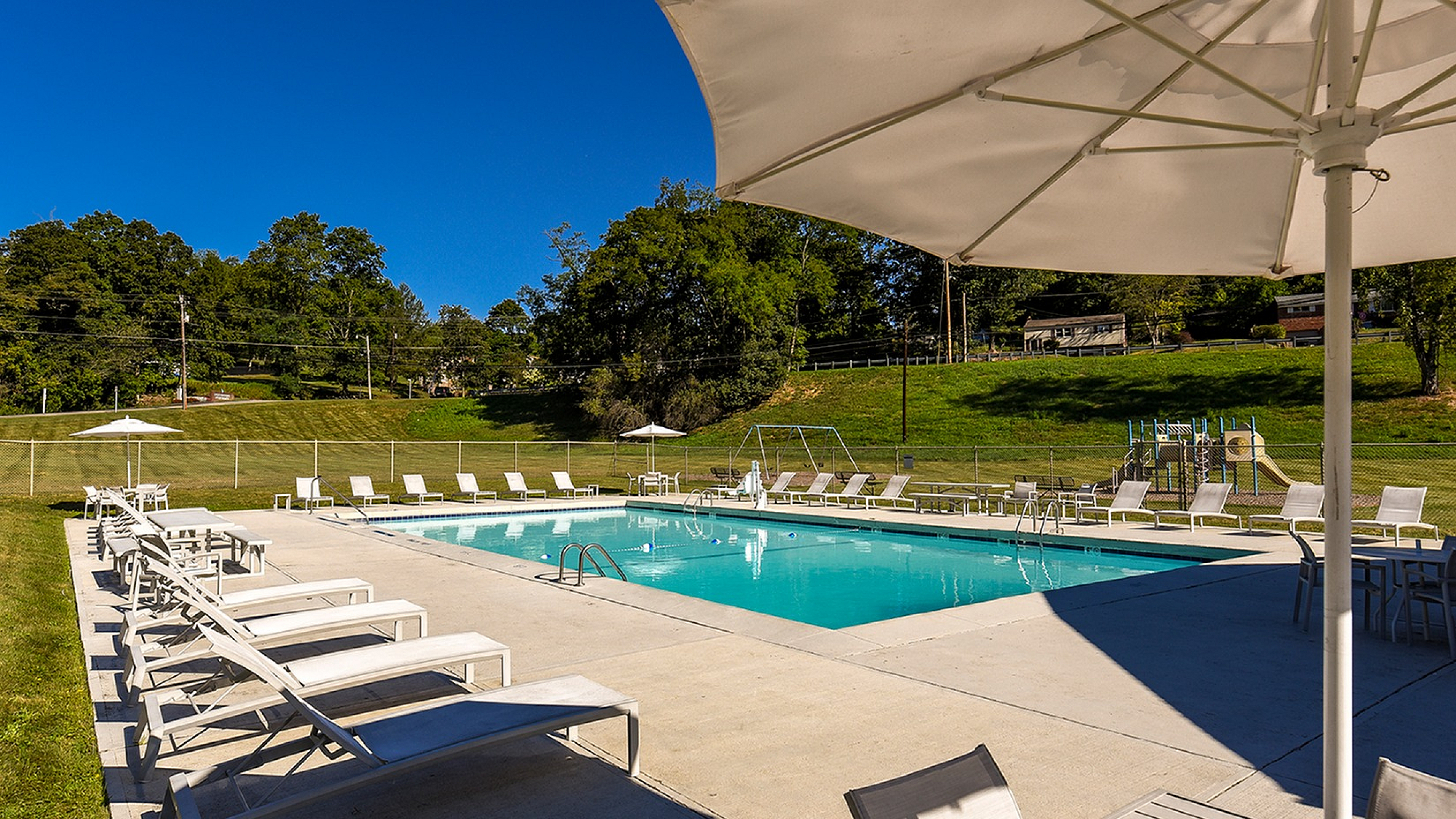 Inviting outdoor swimming pool surrounded by stylish white loungers and sun umbrellas, set against a serene backdrop of lush greenery.