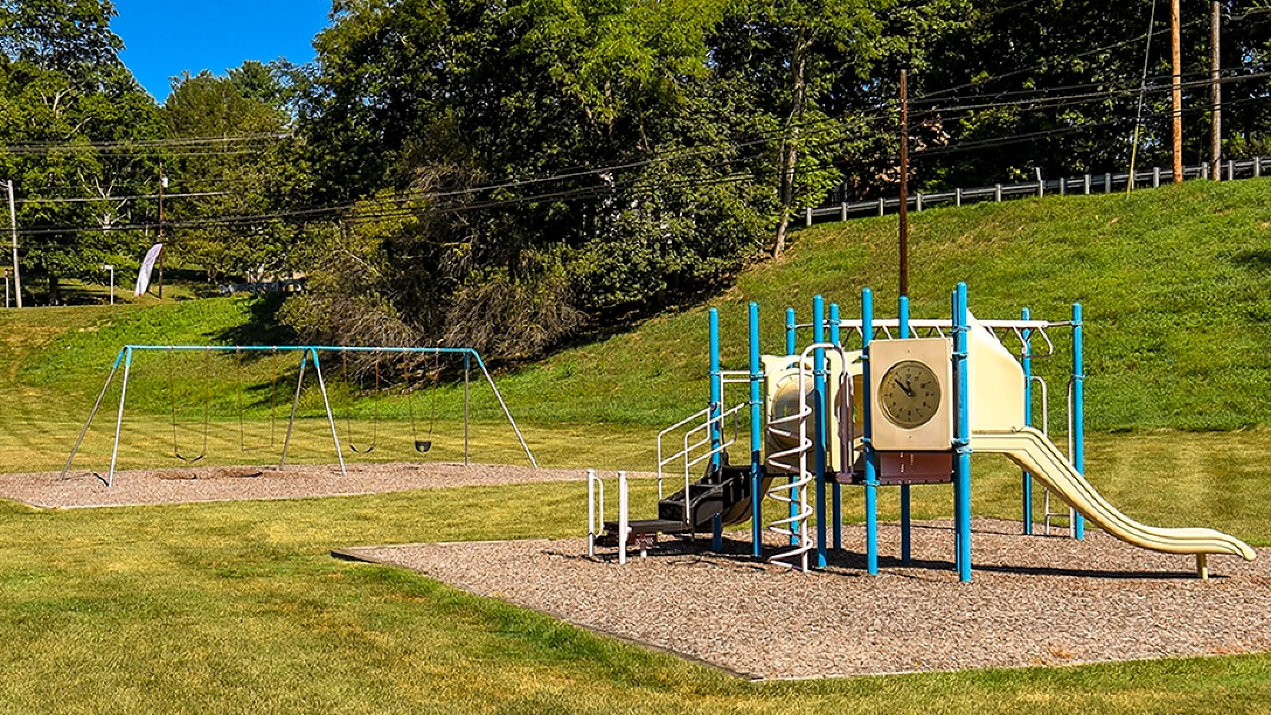 Inviting playground surrounded by lush greenery featuring swings and a colorful slide, perfect for family fun in the sun.