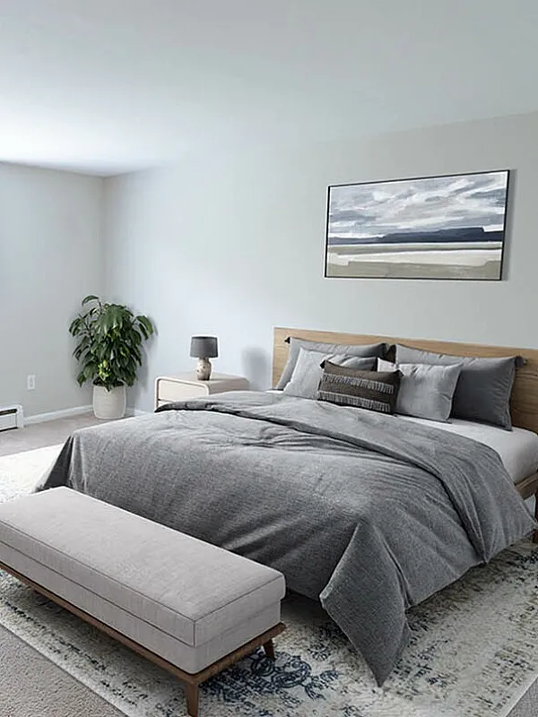 Inviting bedroom with modern decor, featuring a cozy gray bedding set, stylish bedside lamps, and a lush green plant accentuating the serene atmosphere.