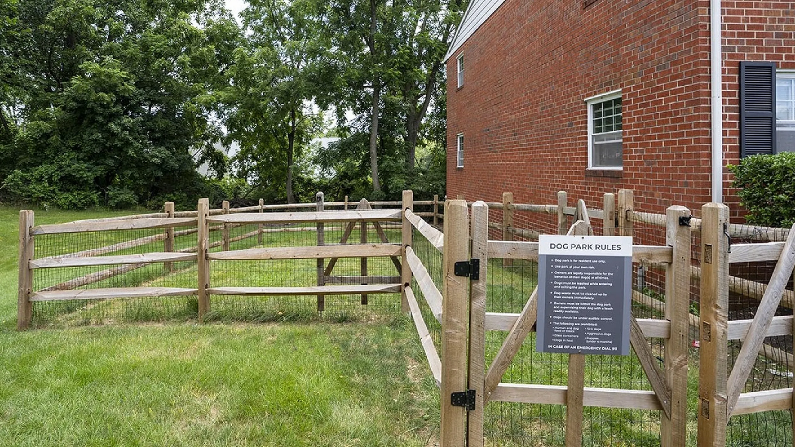 Charming dog park with wooden fencing and lush green grass, nestled beside a brick building, offering a delightful outdoor space for pets to enjoy.