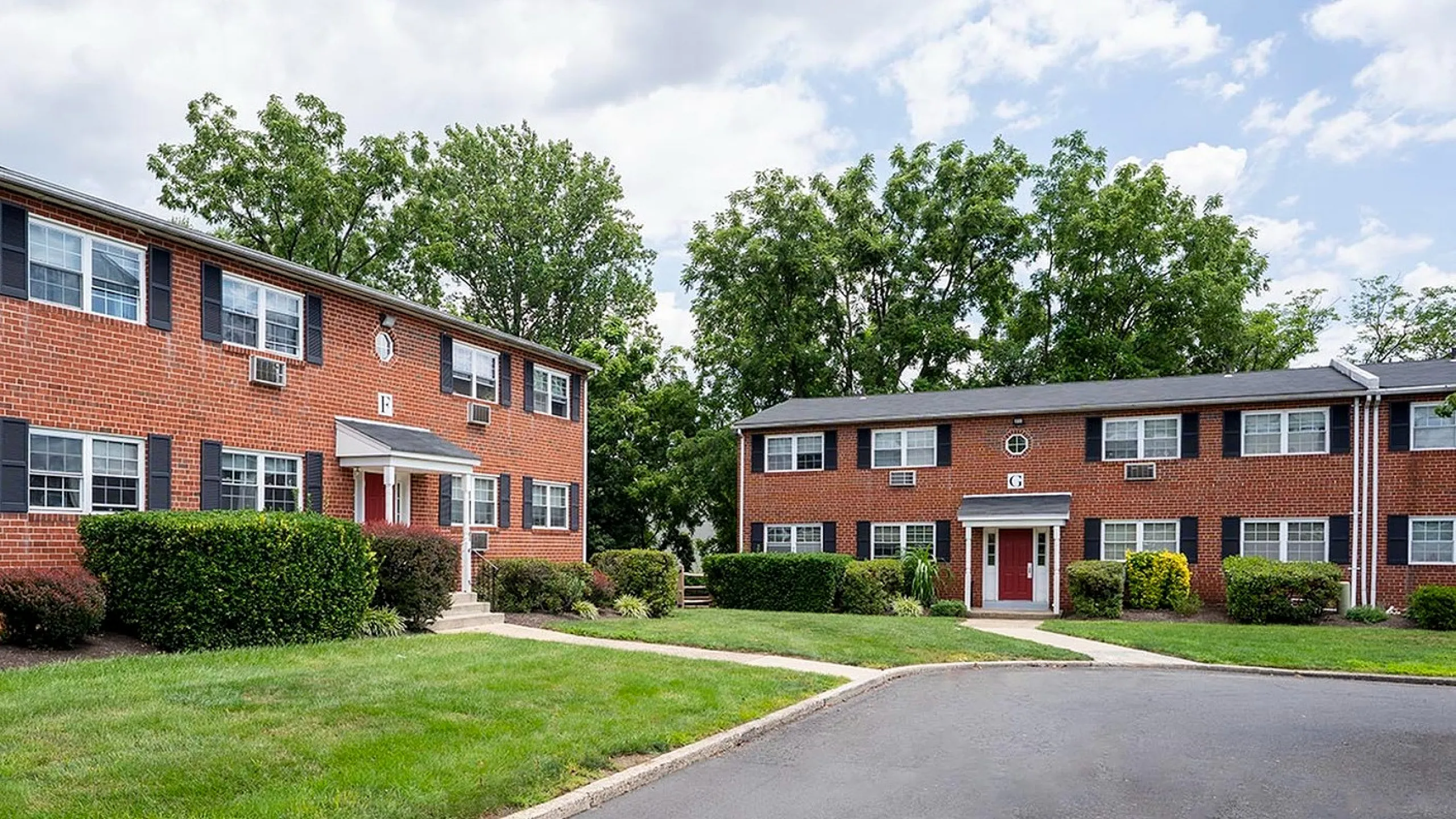 Charming red-brick apartment buildings surrounded by lush greenery, featuring well-maintained pathways and a welcoming outdoor environment.