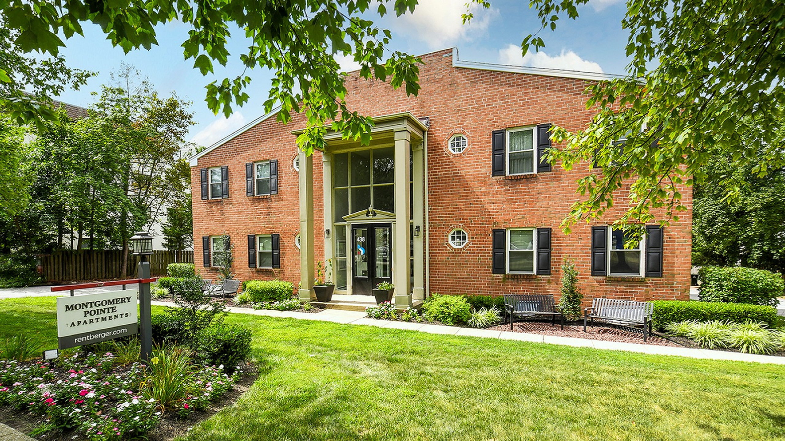 Charming brick apartment building with elegant columns, surrounded by lush greenery and landscaped gardens at Montgomery Pointe Apartments.