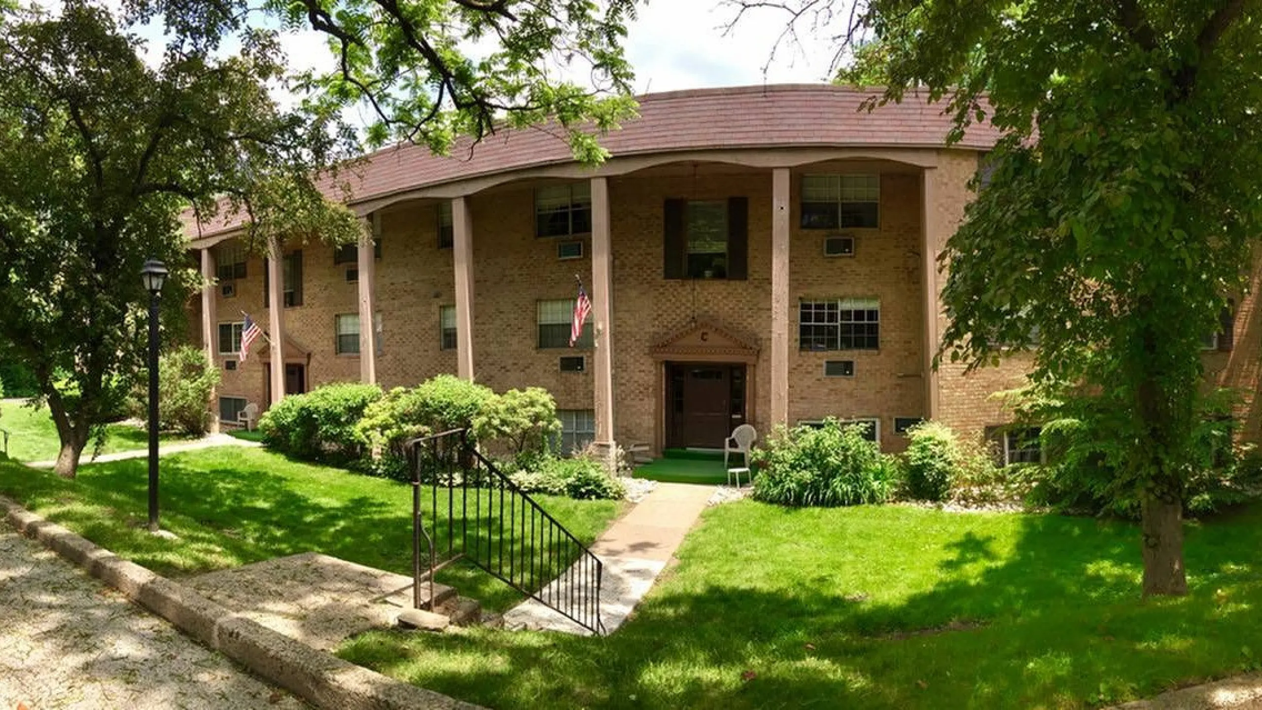 Charming brick apartment building surrounded by lush greenery, offering a serene and inviting atmosphere.