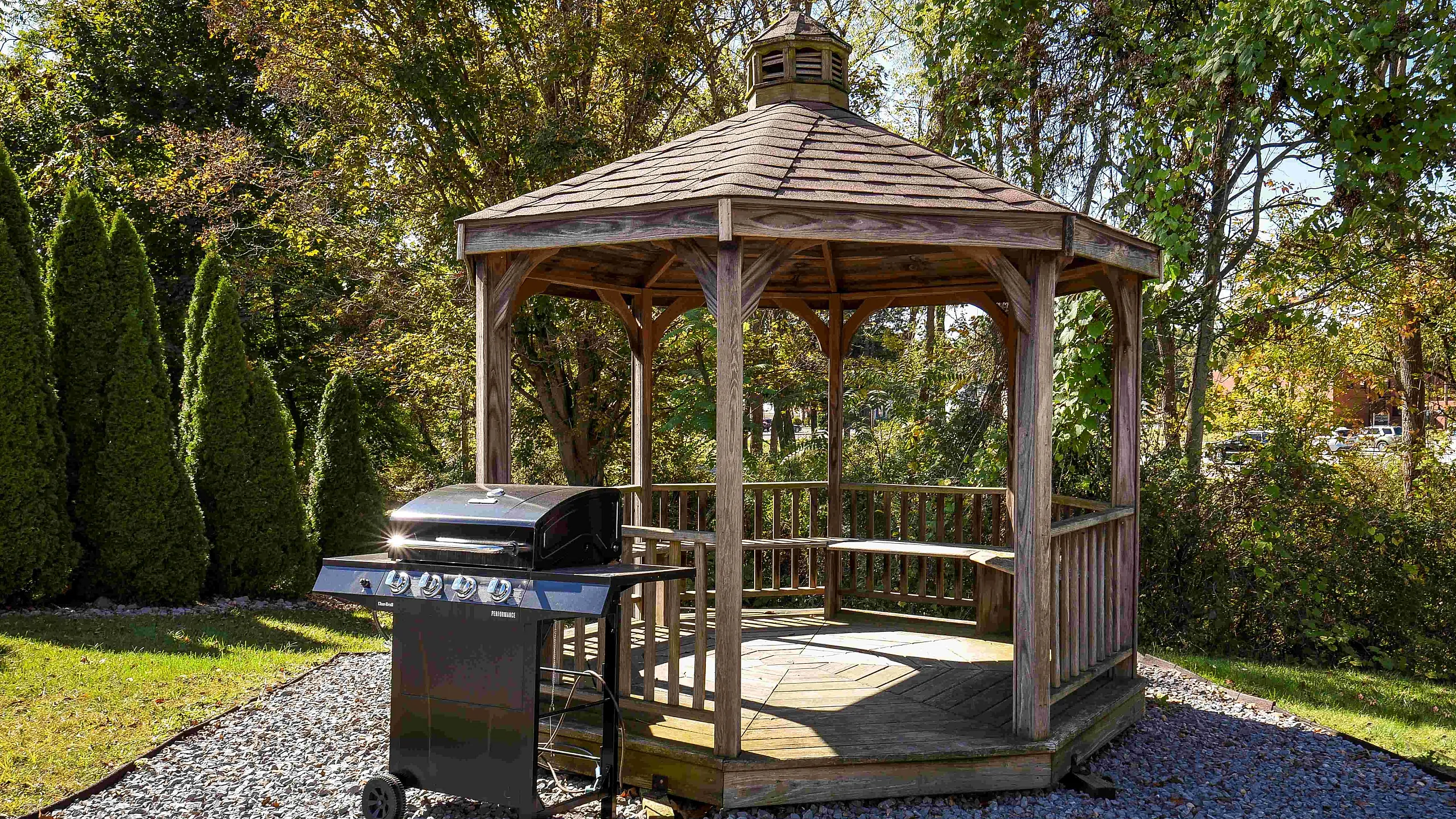 Charming garden gazebo with barbecue grill, surrounded by lush greenery, perfect for outdoor gatherings.