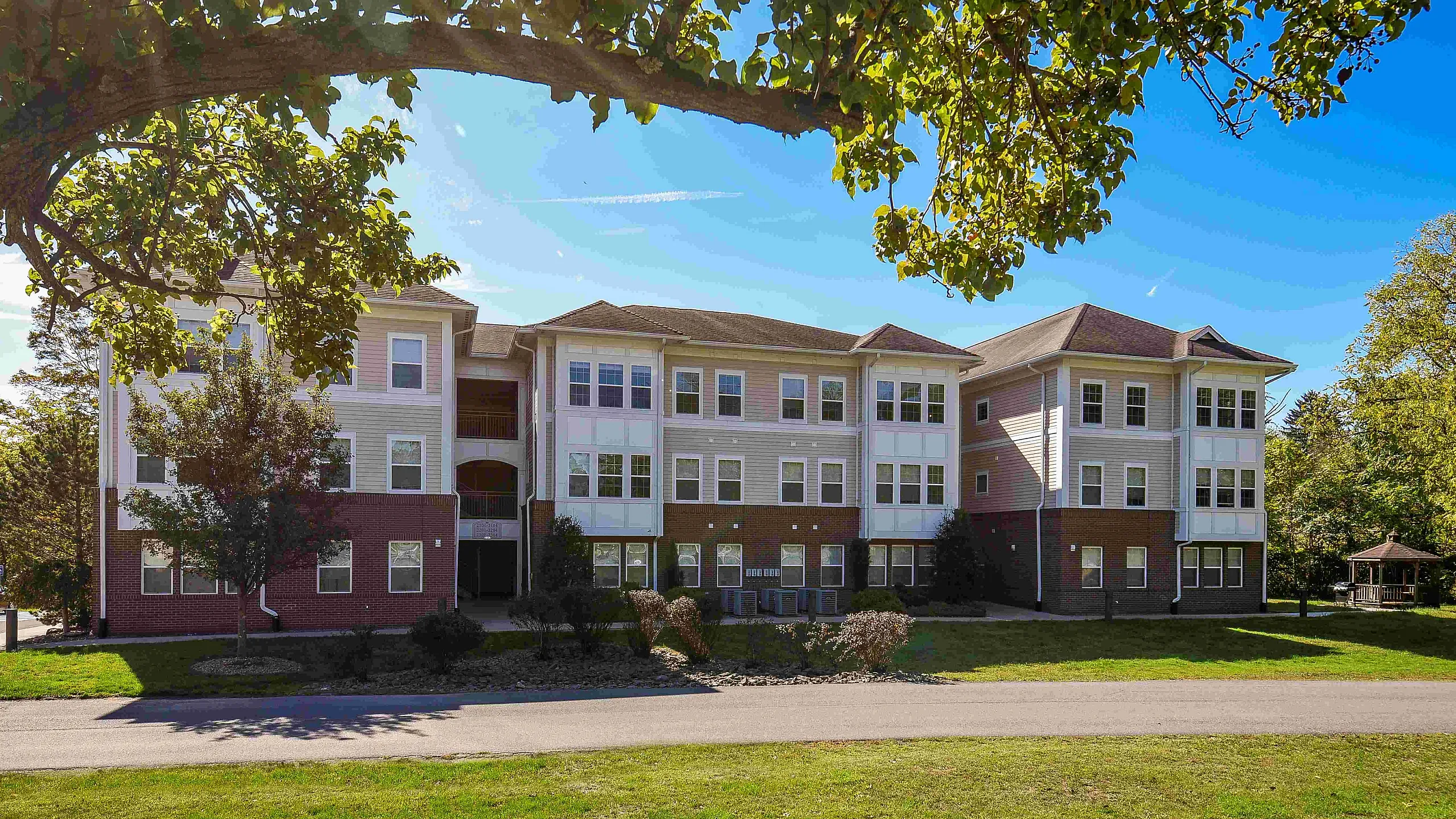 Charming three-story apartment building with modern architecture, nestled in a lush green setting under a bright blue sky.