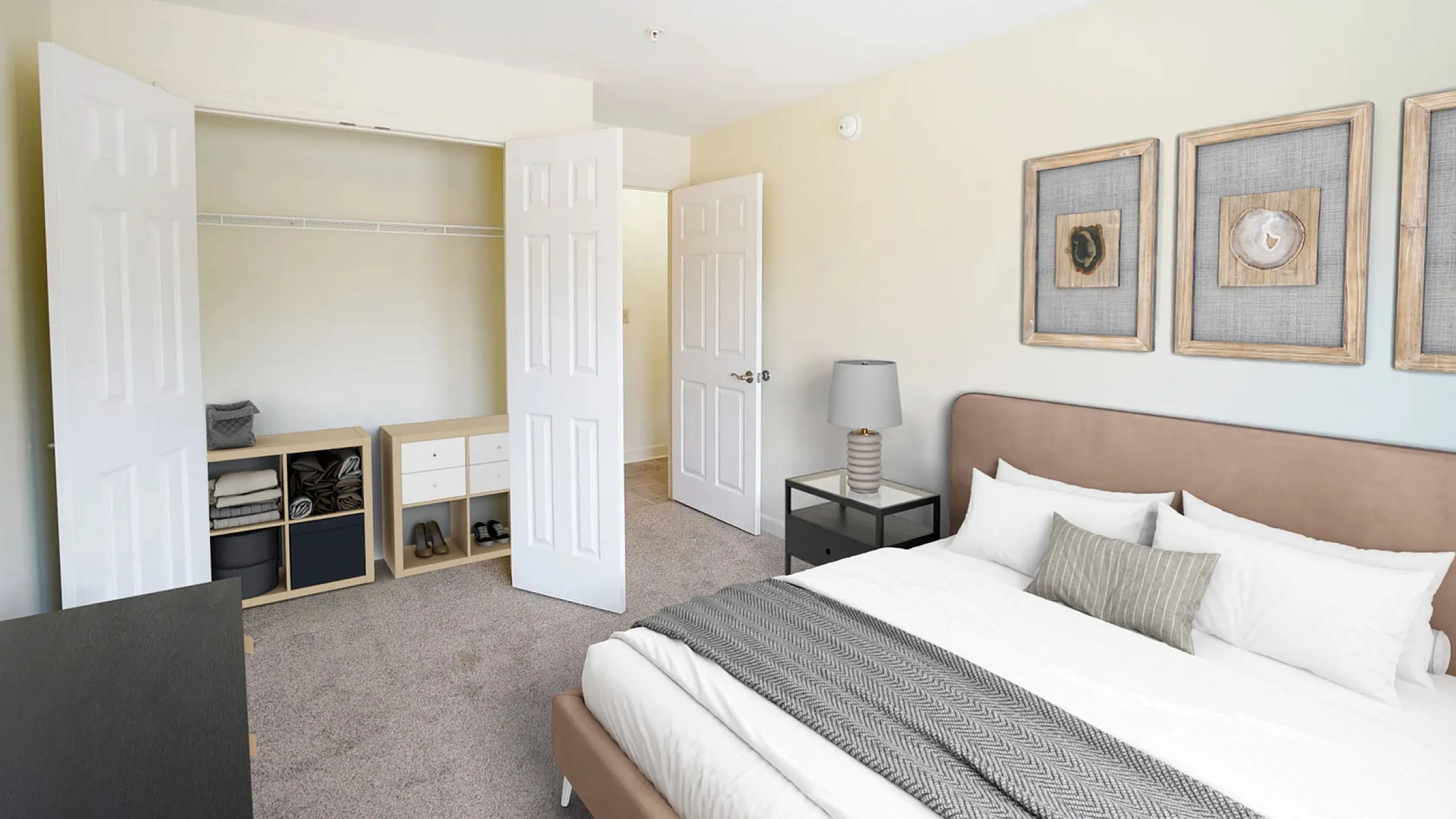 Elegant bedroom featuring plush carpeting, a cozy bed with stylish artwork, ample closet space, and modern lighting.