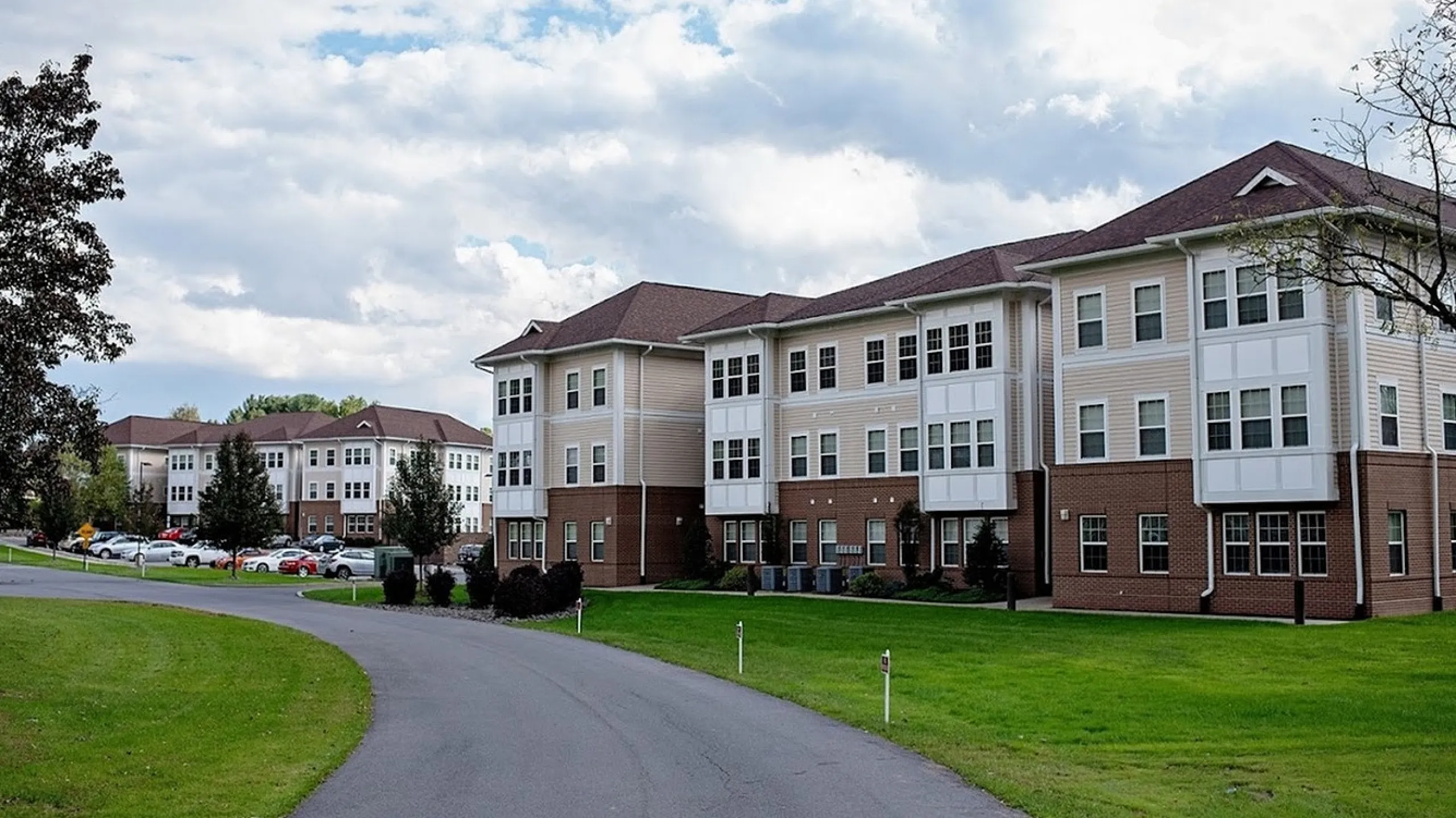 Charming three-story apartment complex with elegant architecture, nestled amidst lush greenery and a scenic driveway.