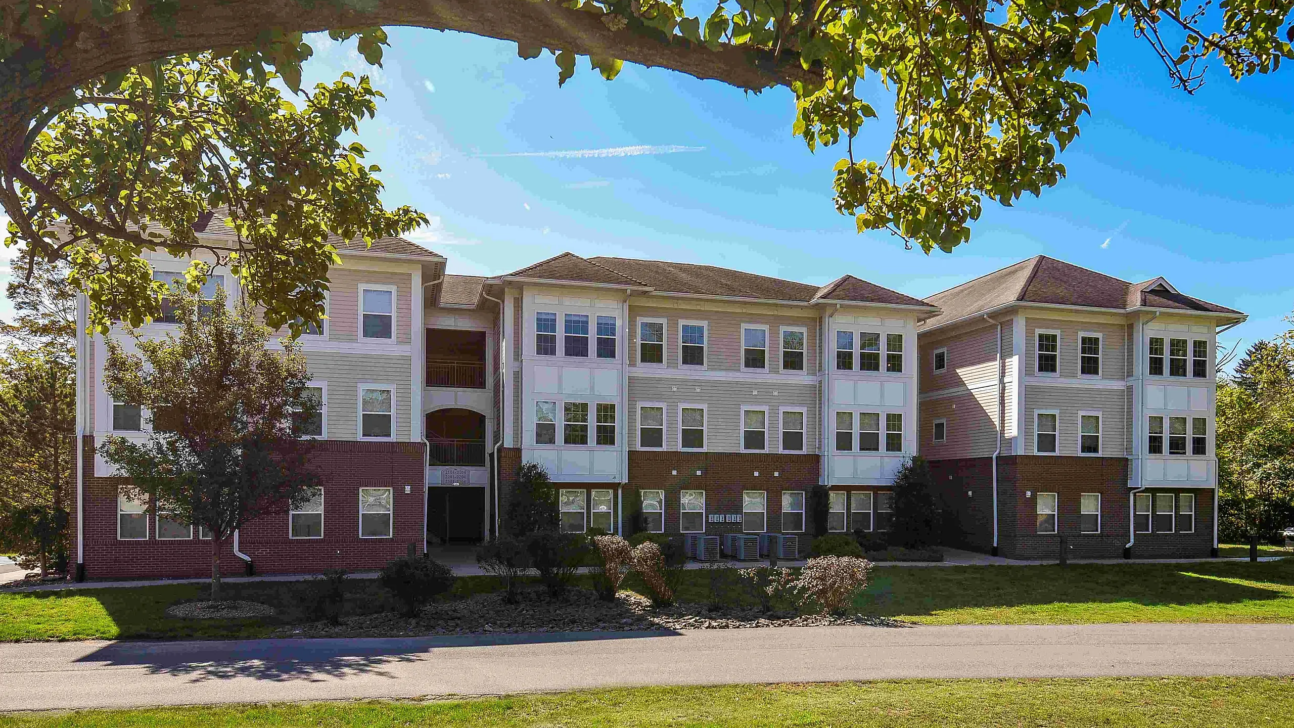 Charming three-story apartment building with a modern design, surrounded by lush greenery and a serene blue sky.