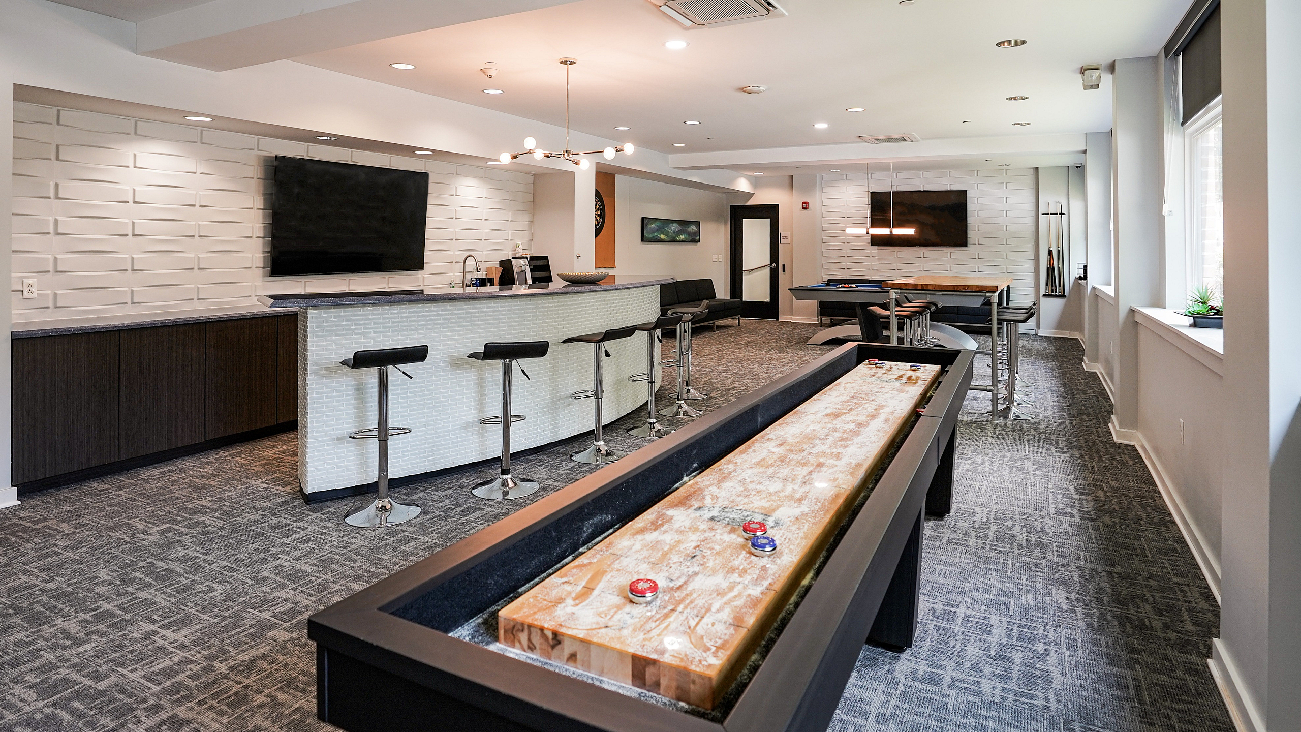 Chic recreation room with modern seating, bar area, and shuffleboard table, perfect for entertainment and relaxation.