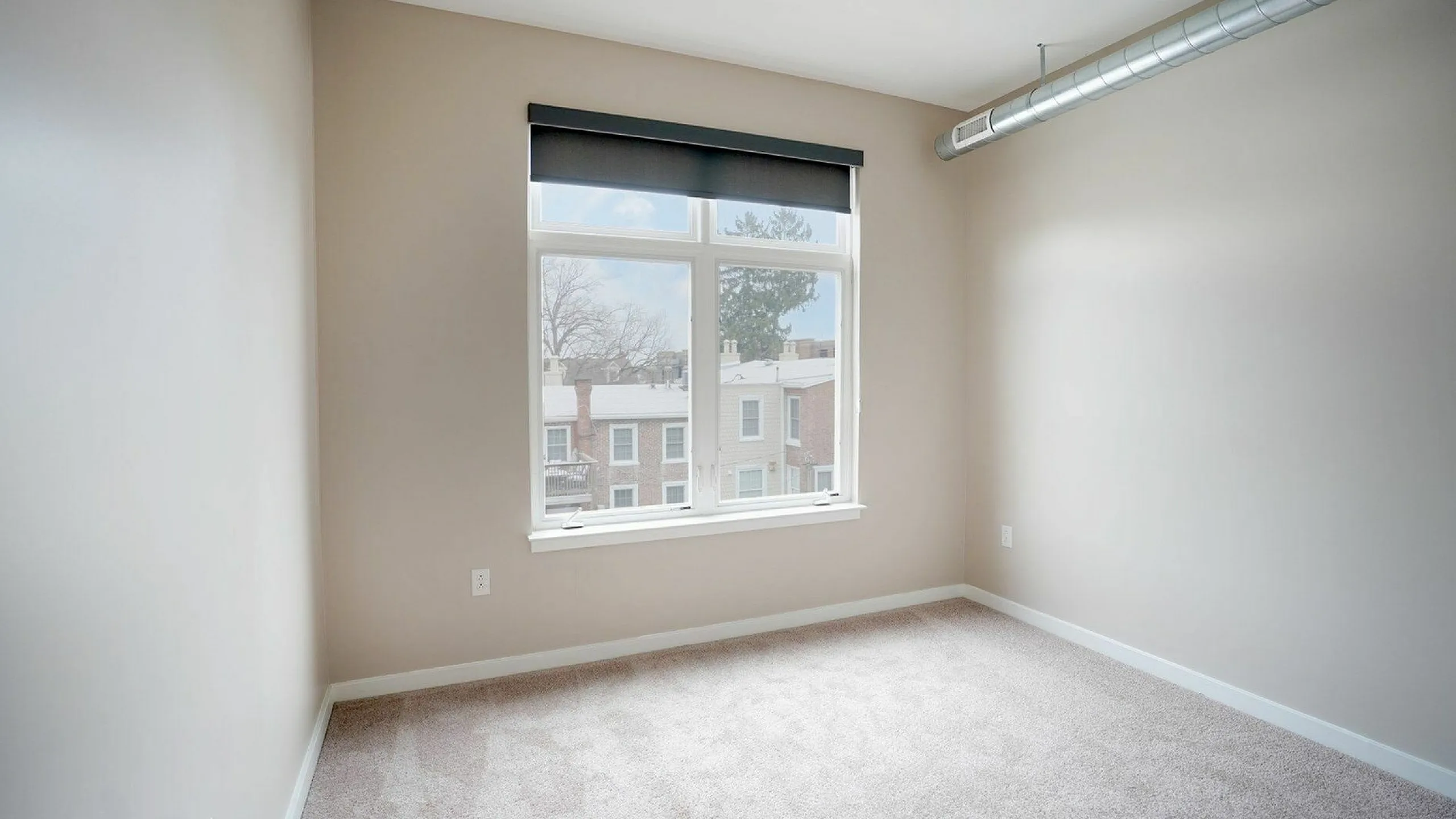 Bright and airy room with large window, neutral walls, and modern exposed ductwork, perfect for relaxation or work-from-home setup.