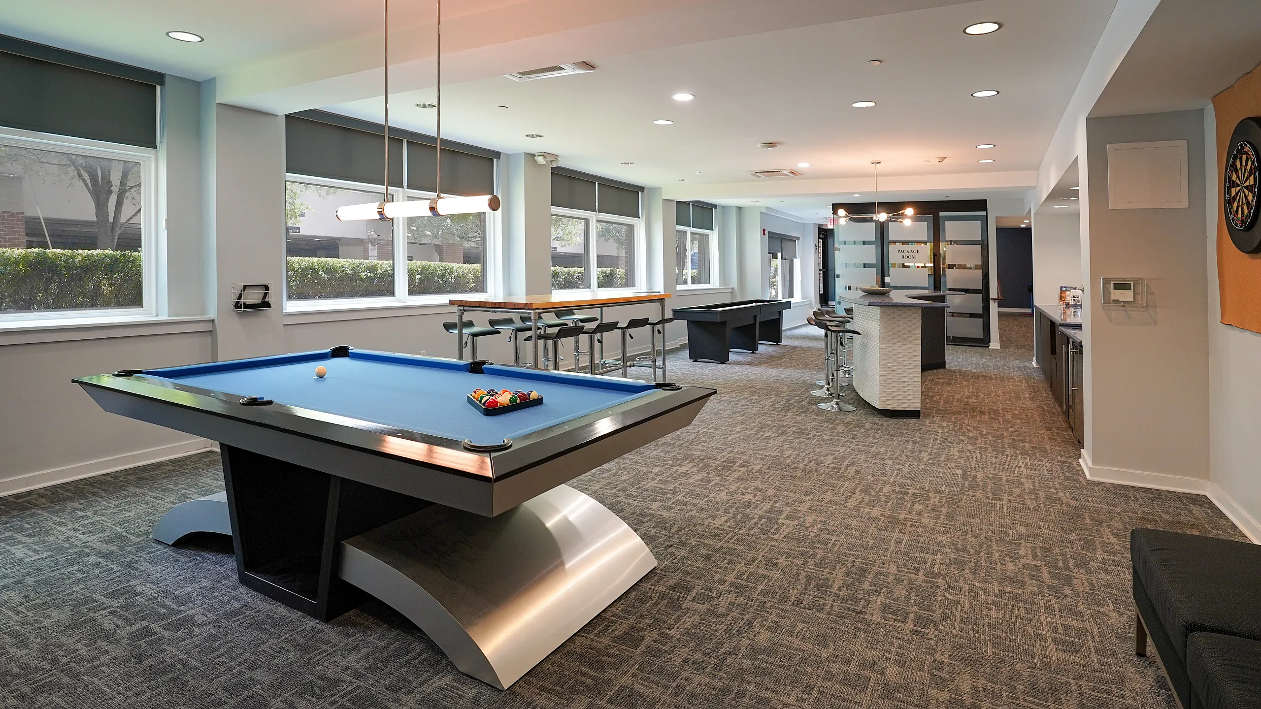 Elegant recreation room featuring a sleek billiards table, modern bar area, and large windows for natural light.