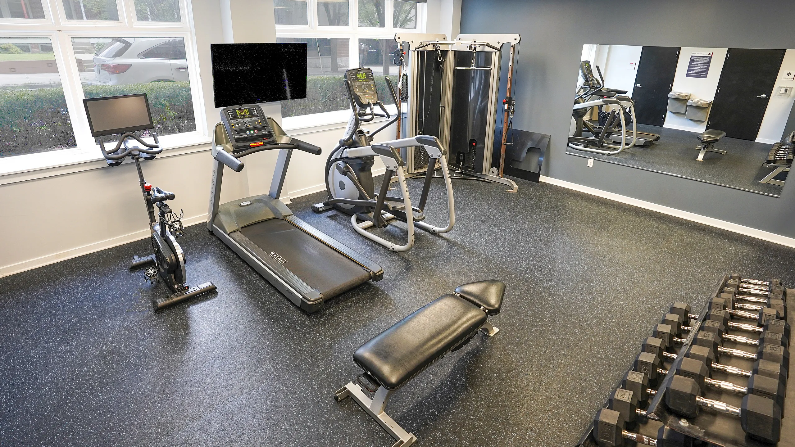 Modern apartment gym with cutting-edge equipment includes treadmill, elliptical, stationary bike, and a full set of free weights, designed for an invigorating workout experience.
