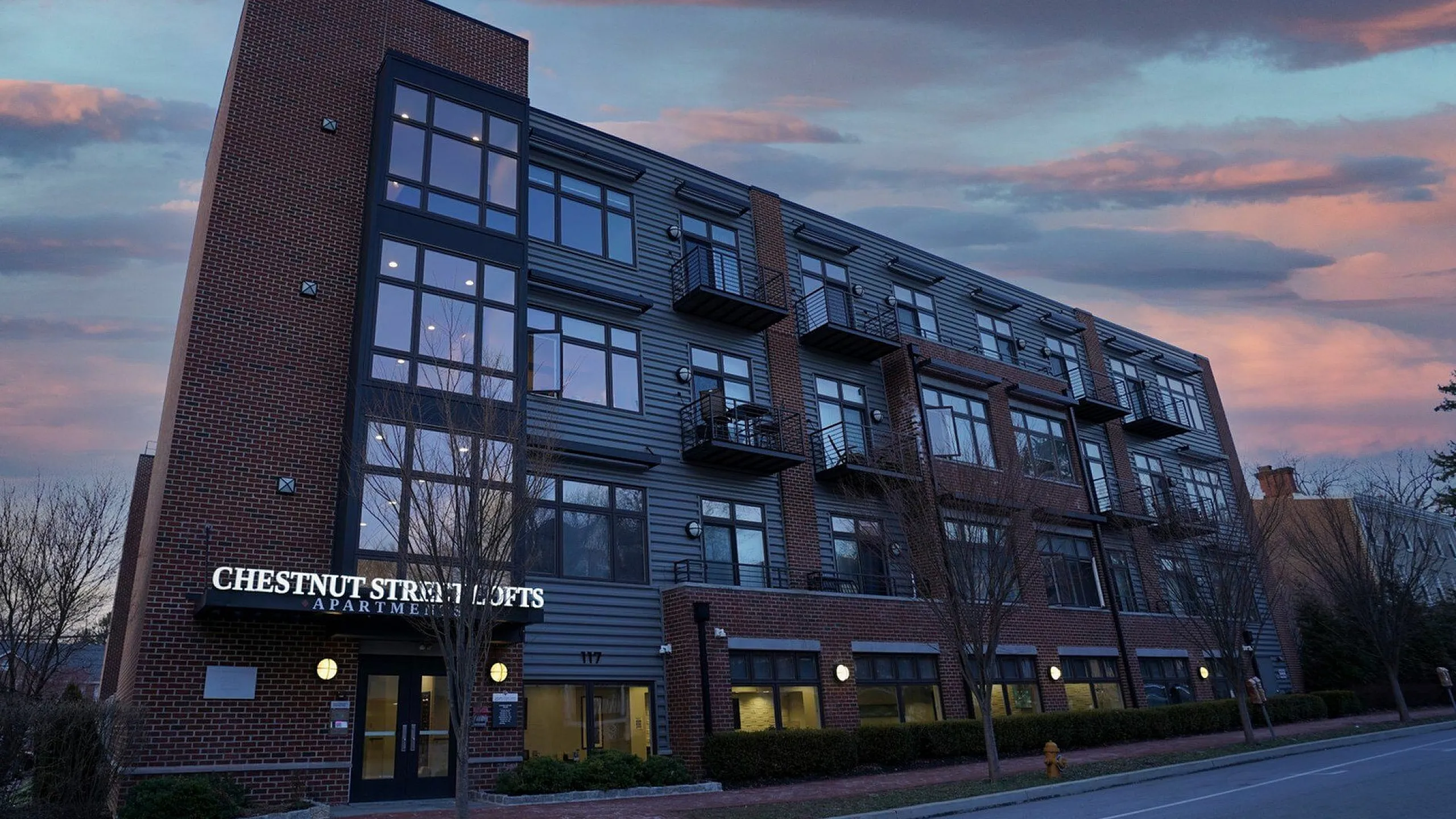 Modern brick apartment building at dusk with sleek metal accents and large windows, featuring Chestnut Street Lofts signage.