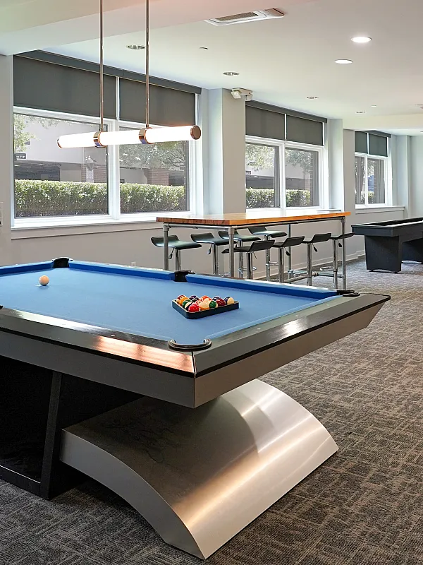 Modern recreation room with a sleek pool table, stylish bar seating, and large windows offering bright natural light.