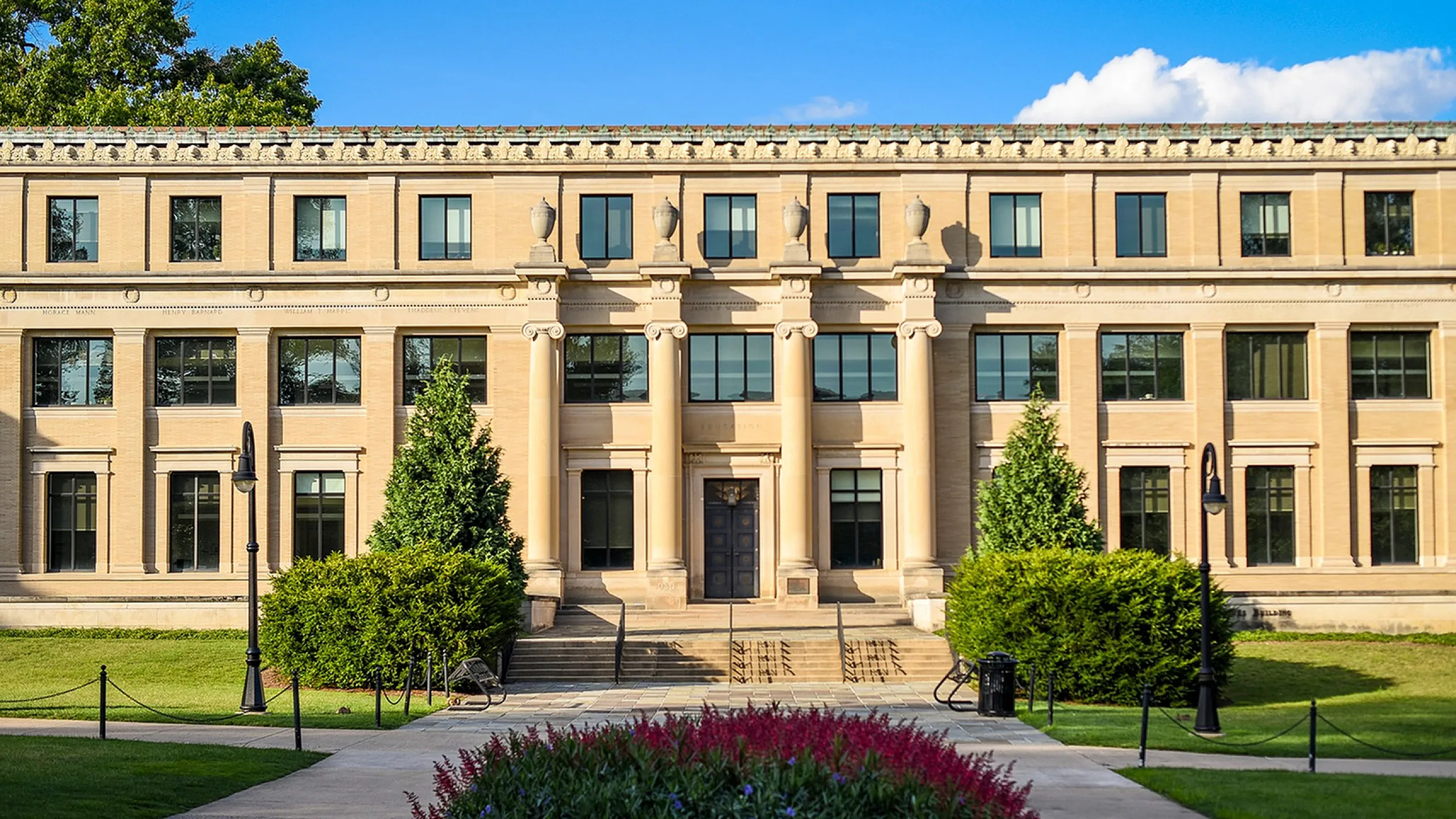 Grand Neoclassical building with impressive columns and lush landscaping on a bright sunny day.