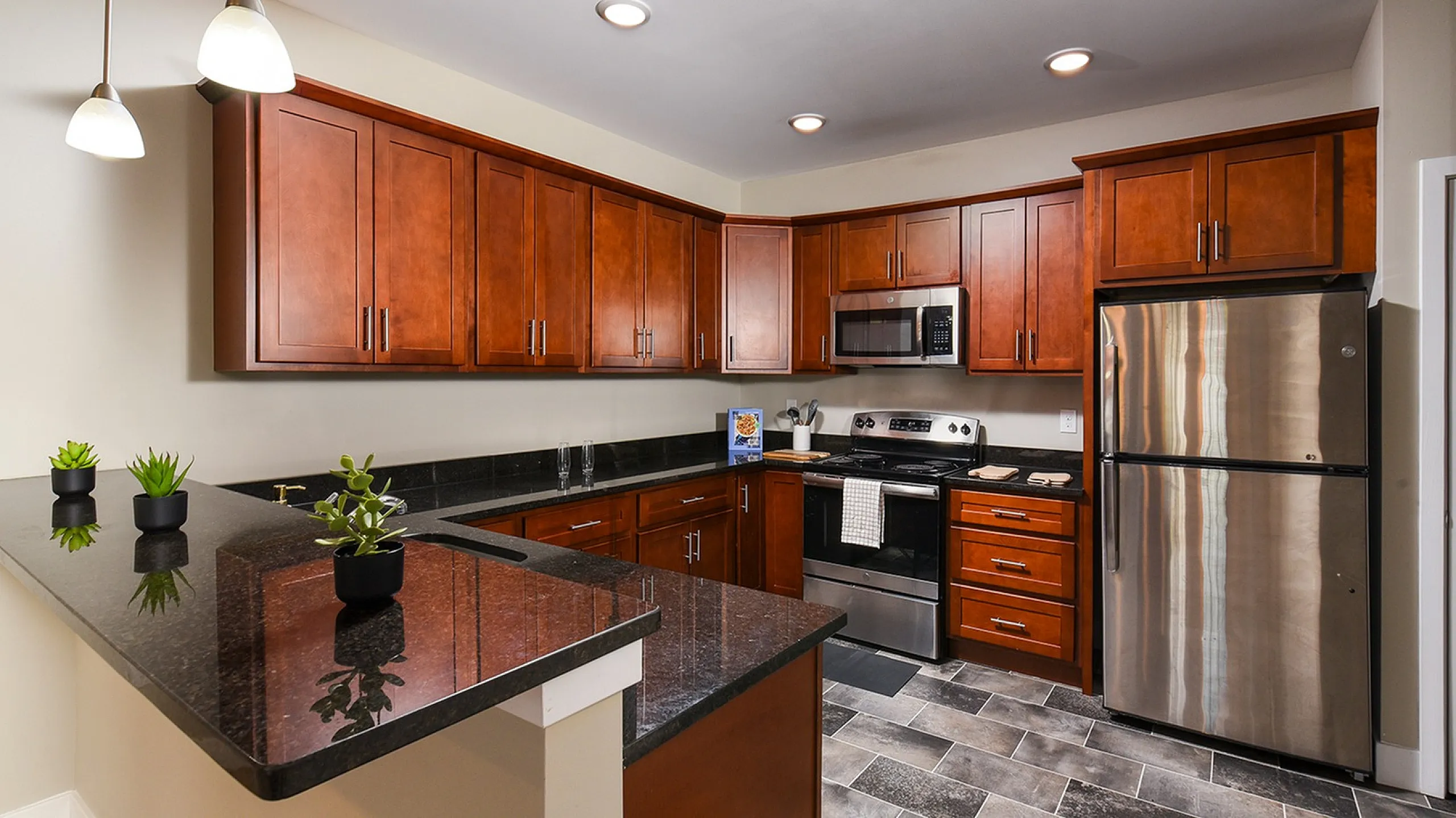 Modern kitchen with sleek granite countertops, rich wooden cabinets, stainless steel appliances, and stylish pendant lighting.