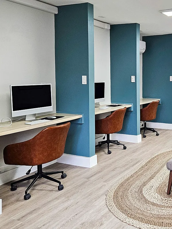 Modern communal workspace with stylish computer stations, ergonomic chairs, and a cozy seating area, optimizing comfort and productivity.