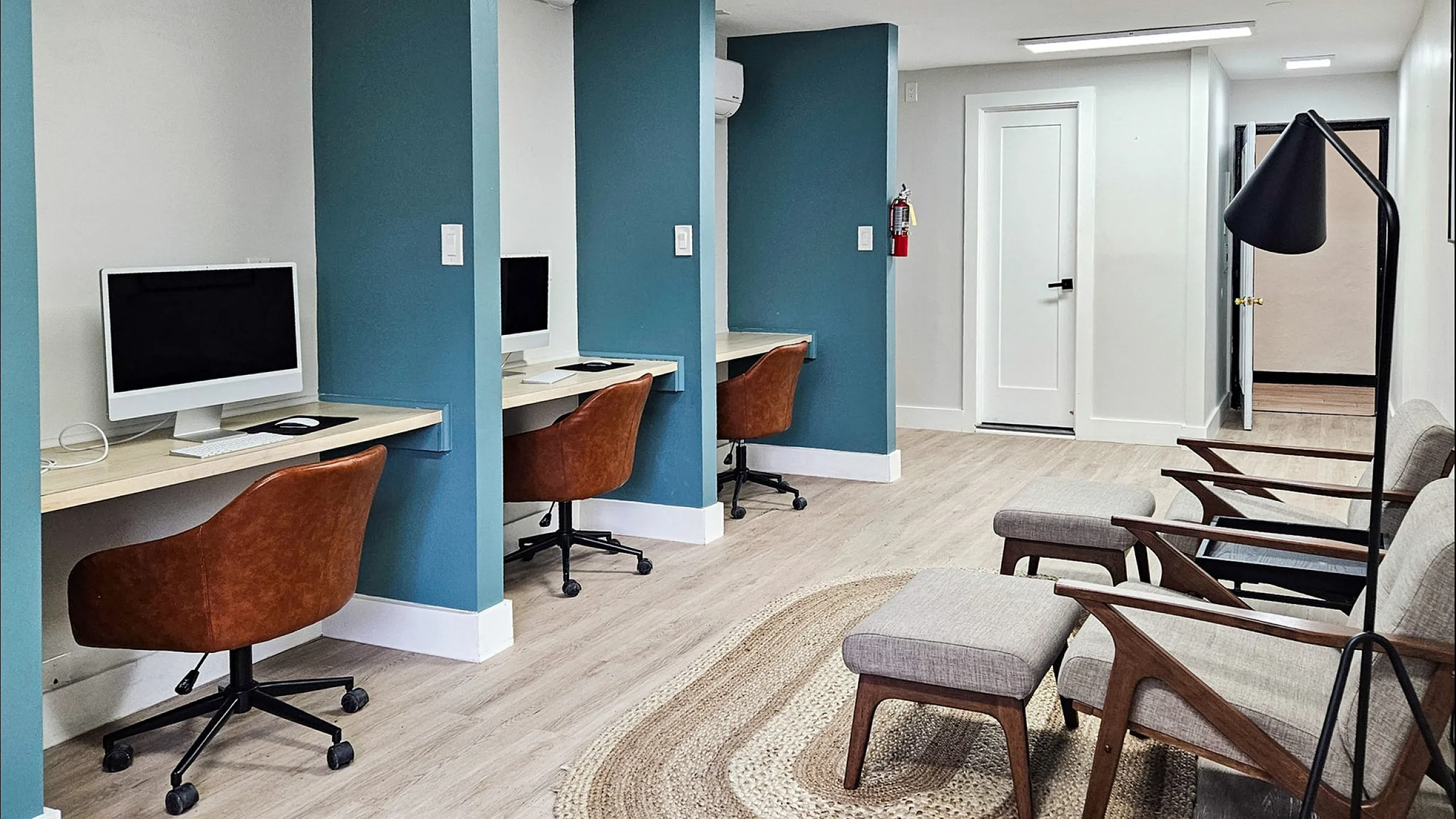 Modern co-working space with individual workstations, ergonomic chairs, and a cozy seating area. Features stylish decor and ample natural light.