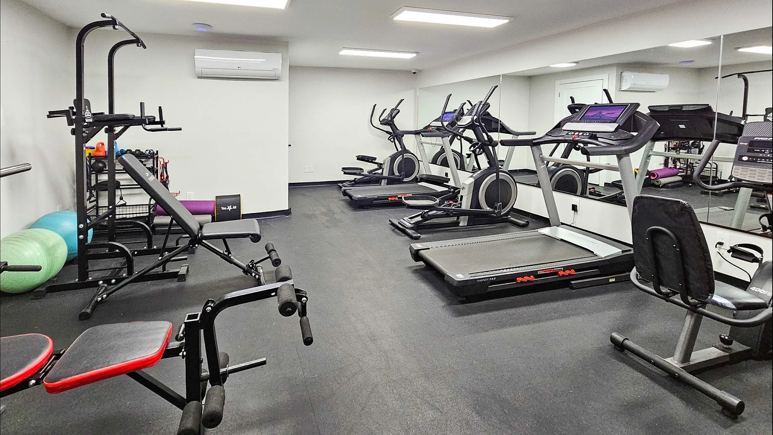 Modern apartment gym featuring state-of-the-art fitness equipment, including treadmills, weights, and exercise mats, in a well-lit space with mirrored walls.