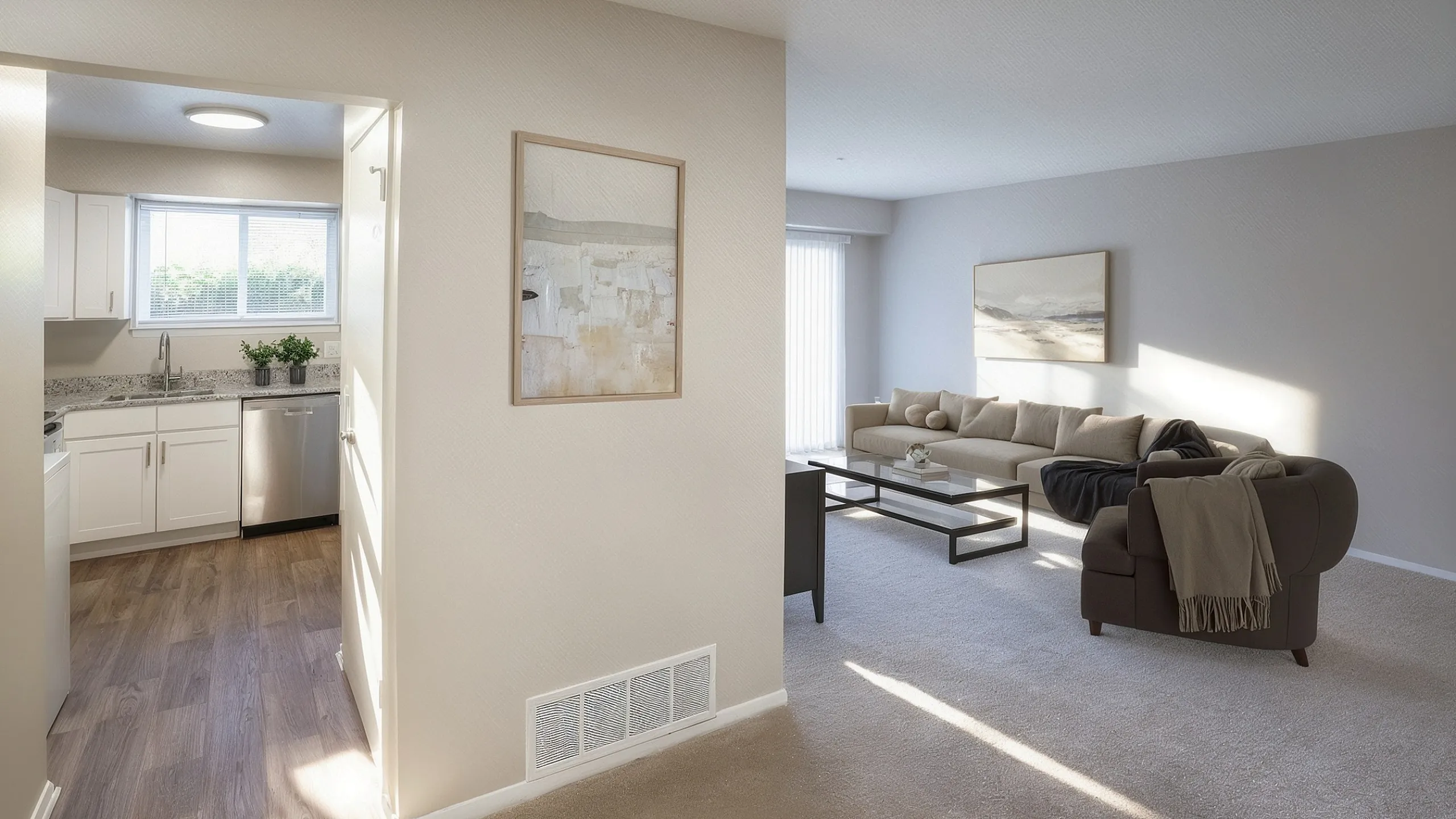Cozy living space with plush carpet flooring and modern furniture leading to a bright kitchen with sleek cabinetry and stainless steel appliances.