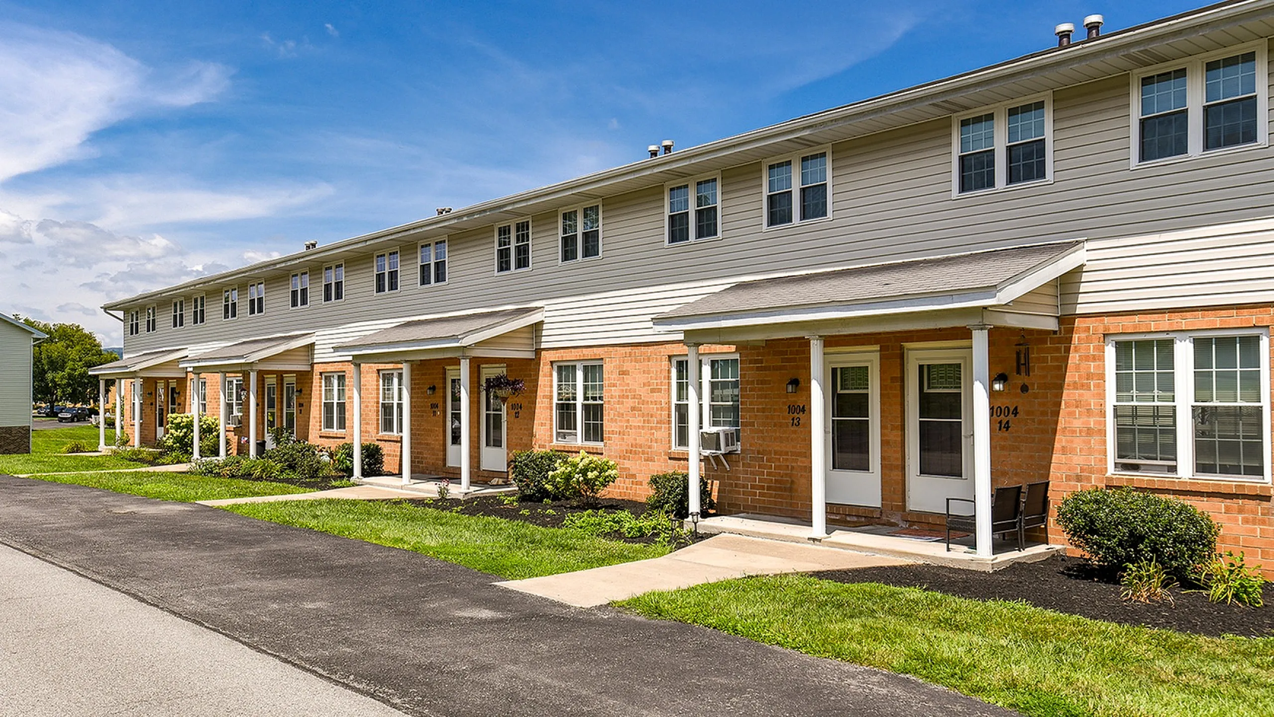 Charming brick townhouses with inviting porches and well-maintained landscaping under a bright blue sky.