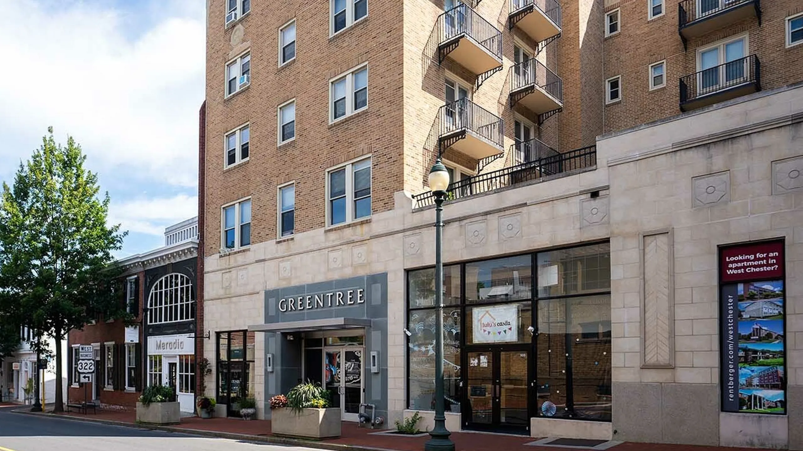 Charming urban brick building with modern balconies, featuring Greentree signage and inviting storefronts, ideal for vibrant city living.