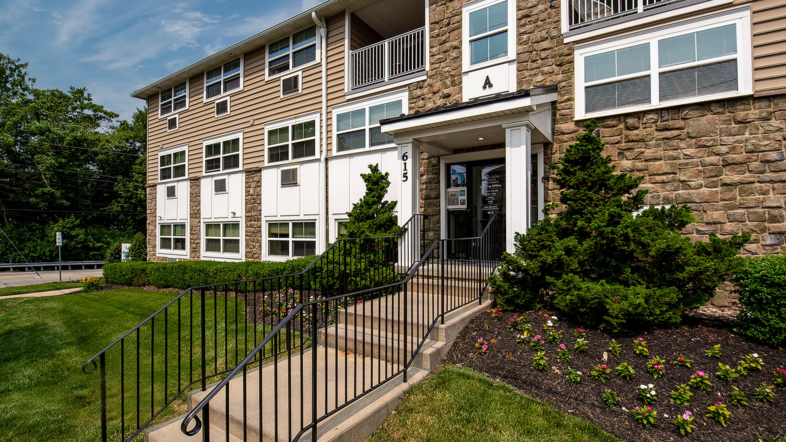 Charming apartment building facade with stone accents, lush landscaping, and inviting entrance.