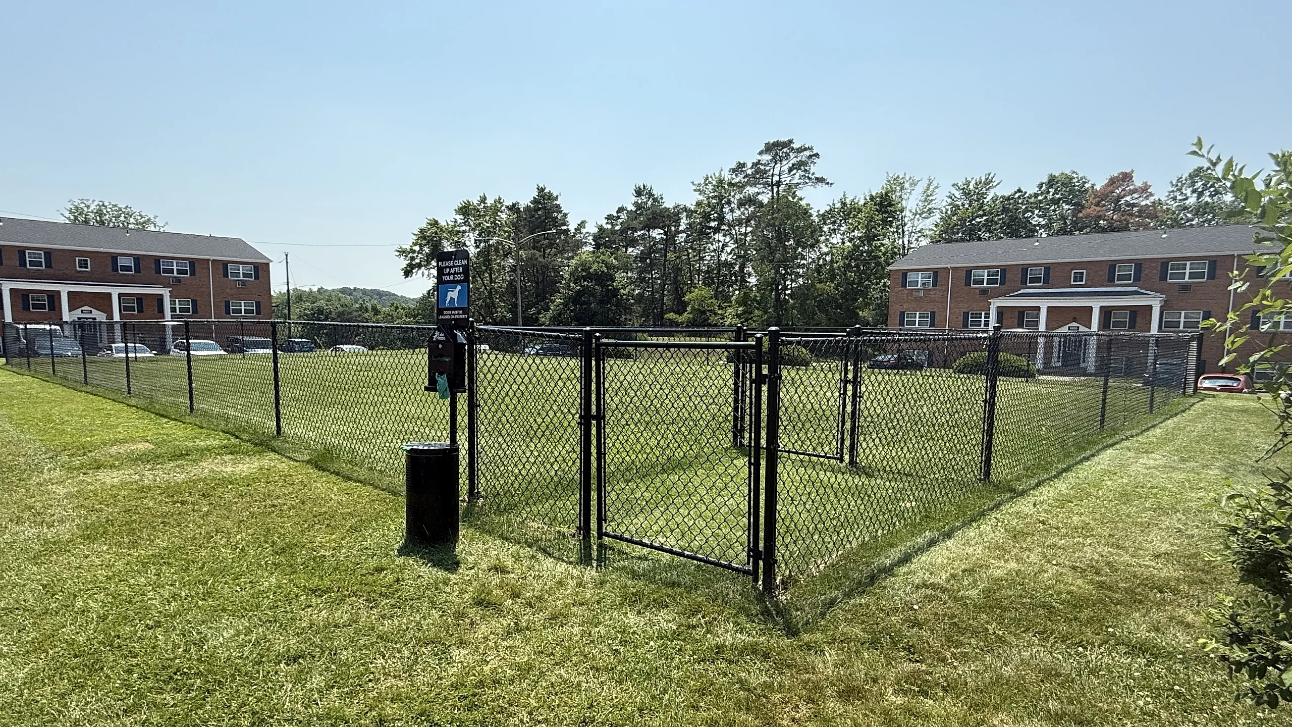 Charming community view with brick buildings and a lush fenced dog park, perfect for pet lovers.