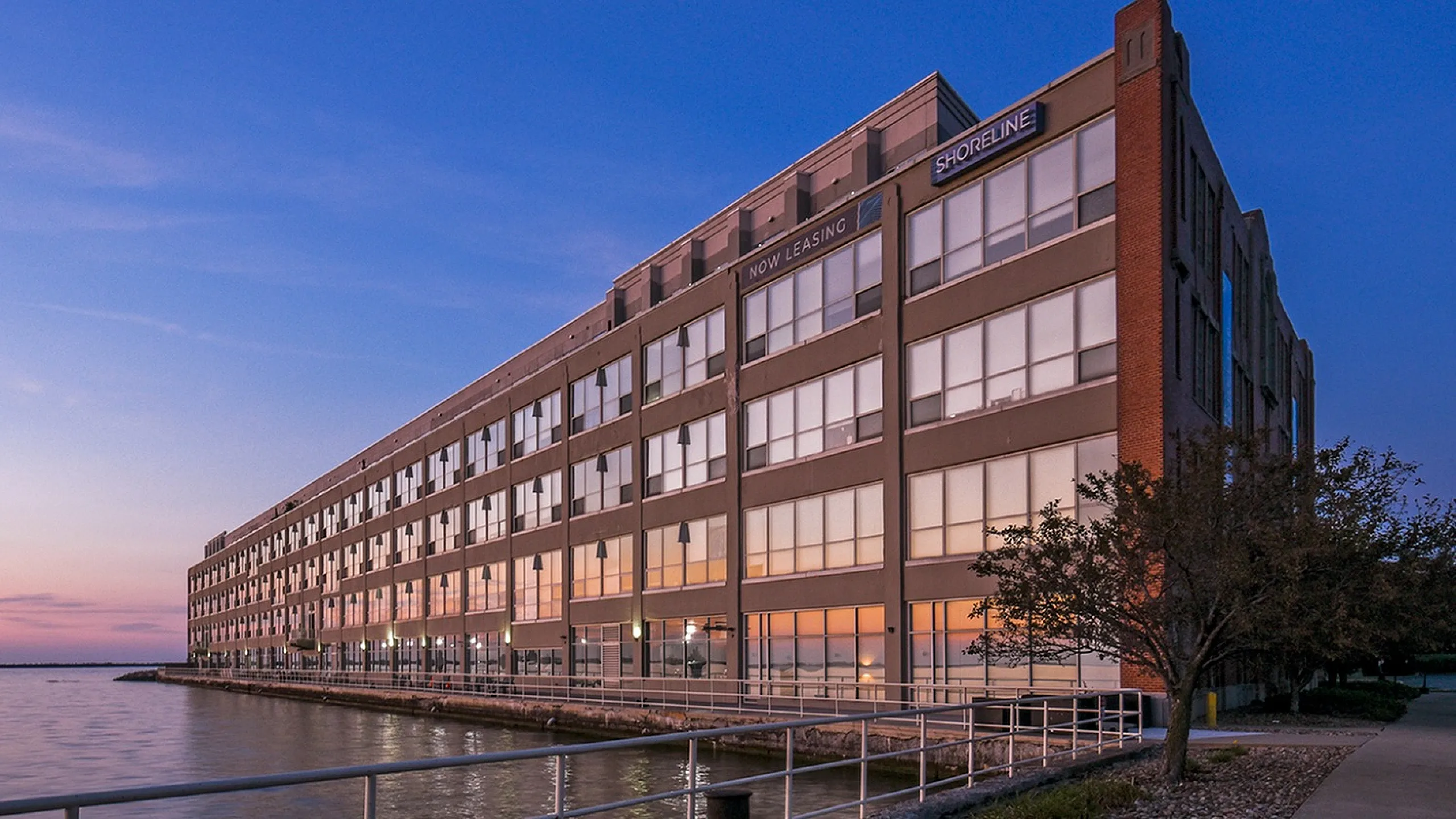 Charming waterfront apartment building at sunset with large windows reflecting the serene lake view.