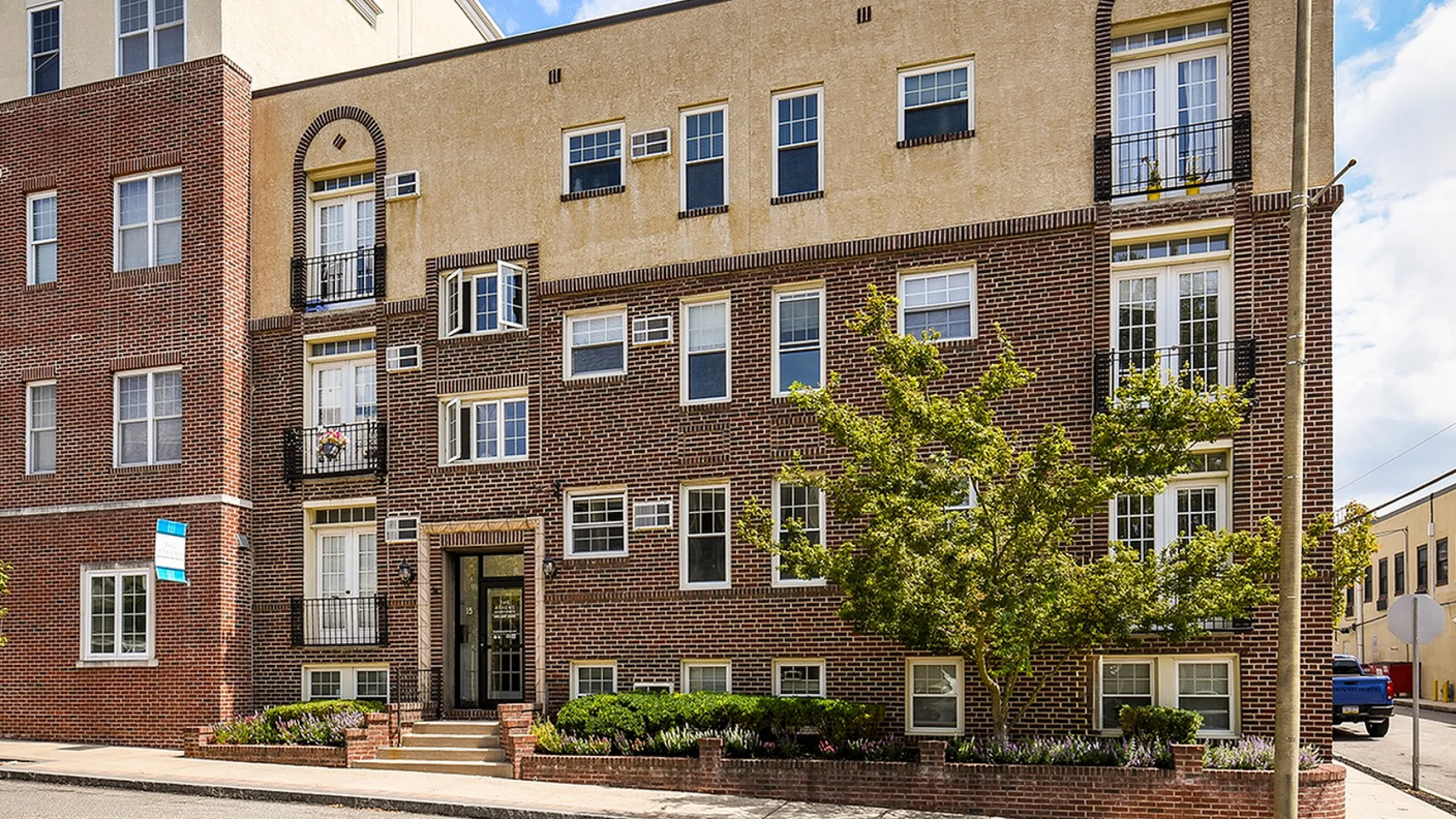 Charming apartment building with classic brick facade, large windows, and lush greenery enhancing curb appeal.