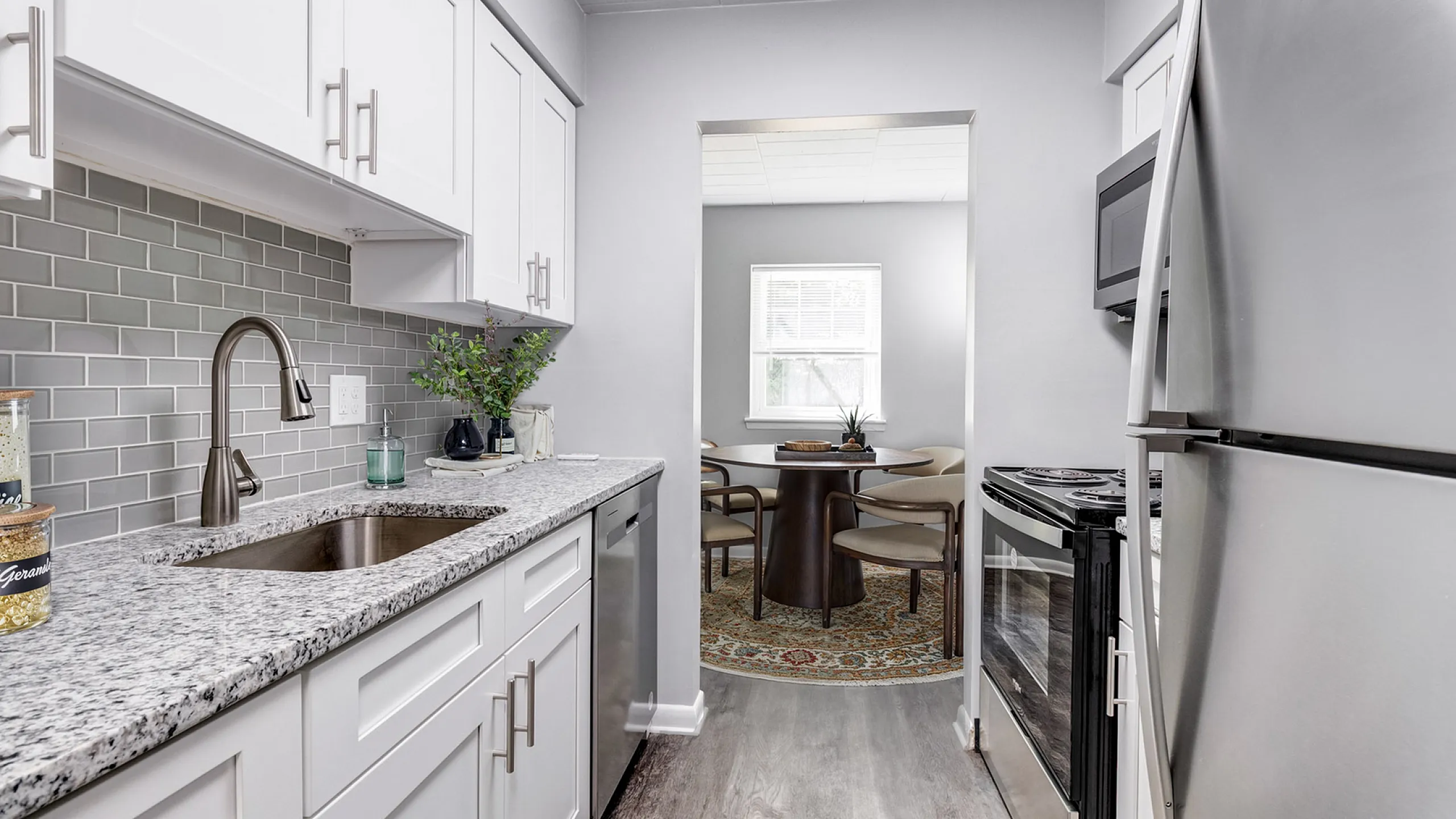 Sleek modern kitchen with stainless steel appliances, granite countertops, and white cabinetry leading to a cozy dining area.