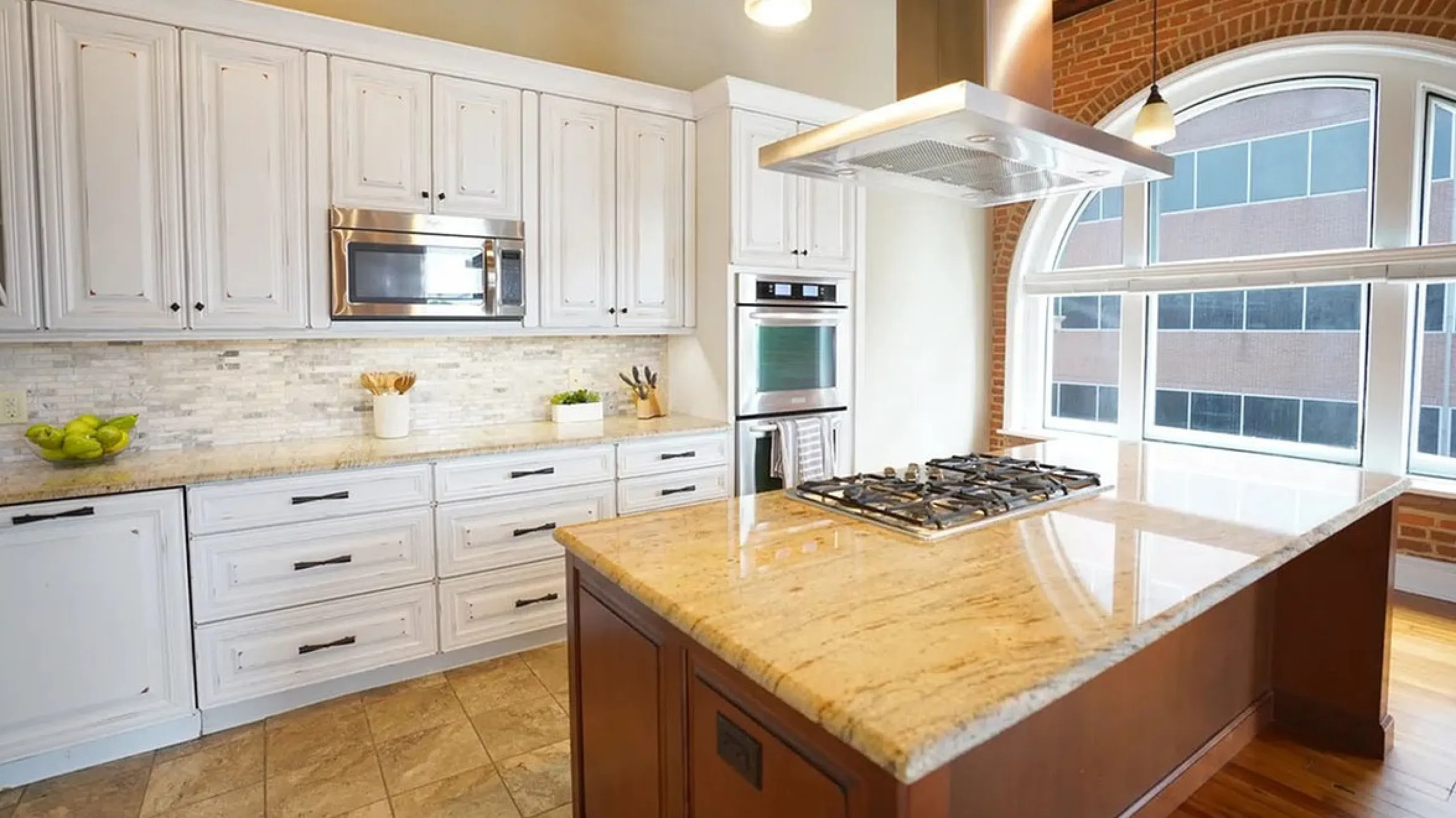 Elegant kitchen with large granite island, modern appliances, and abundant natural light from arched windows.