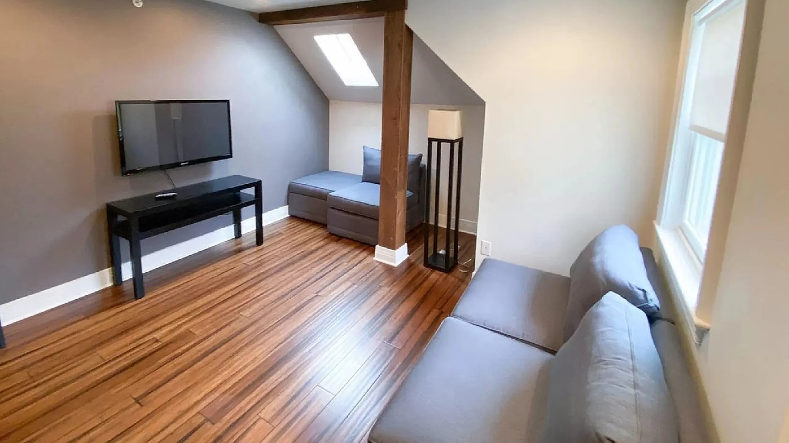 Cozy living room with modern decor, featuring sleek hardwood floors, a wall-mounted TV, and stylish gray seating under ambient lighting.
