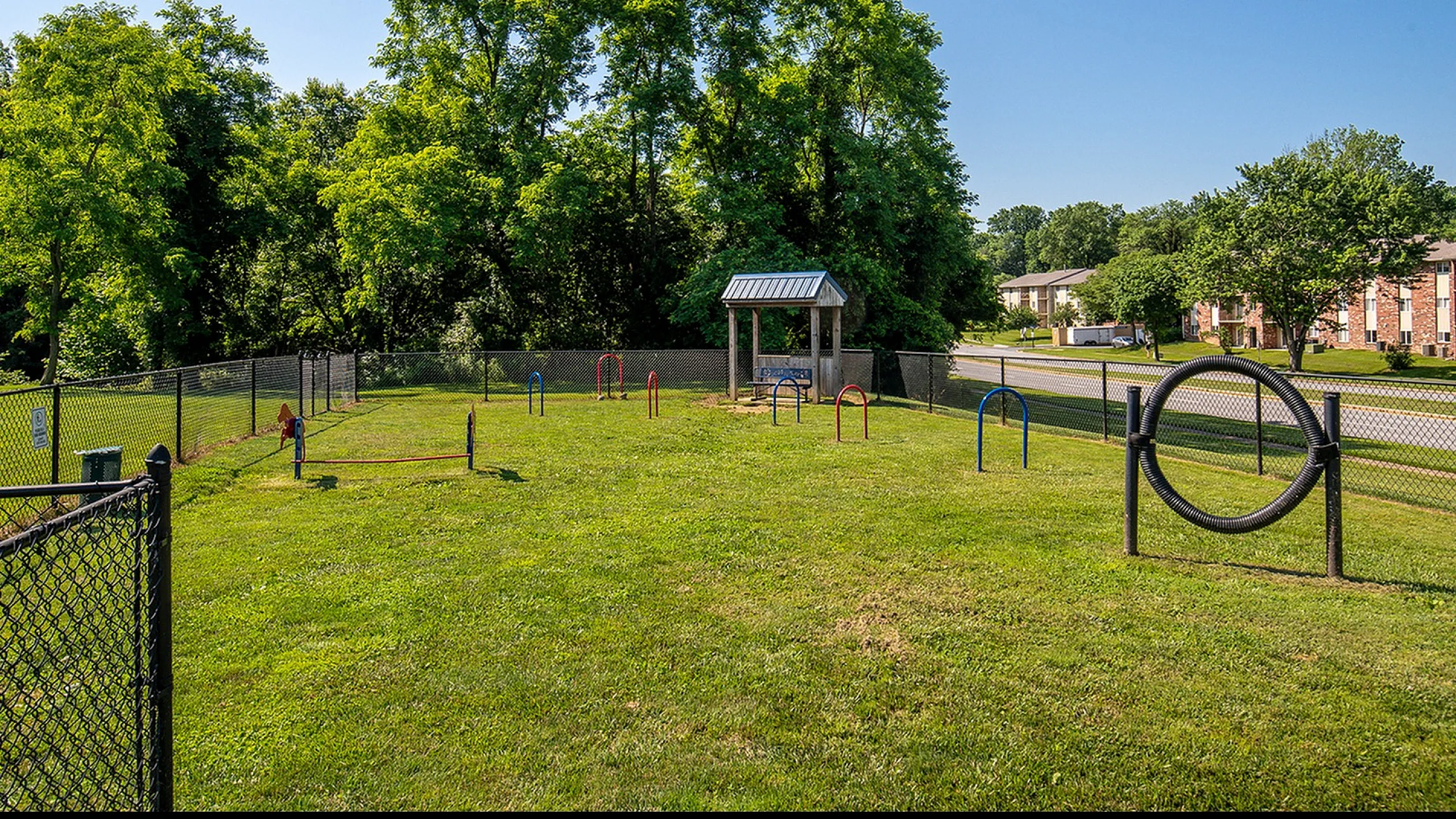 Charming fenced-in dog park with agility equipment surrounded by lush greenery, perfect for pet-friendly community living.