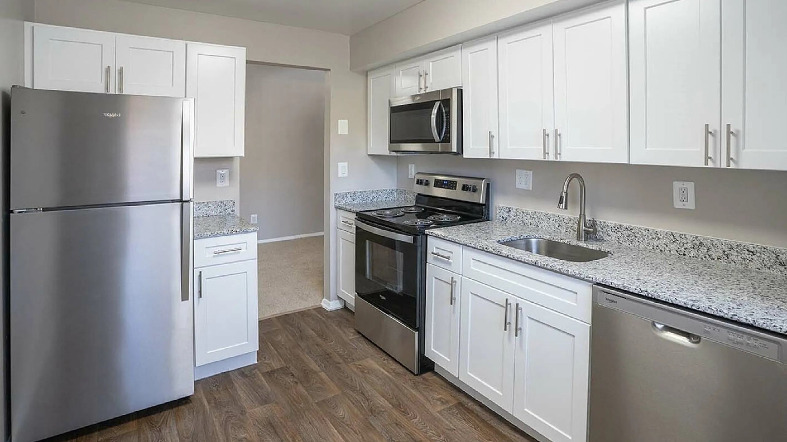 Modern kitchen showcasing sleek stainless steel appliances, elegant granite countertops, and stylish white cabinetry with a contemporary wood floor finish.