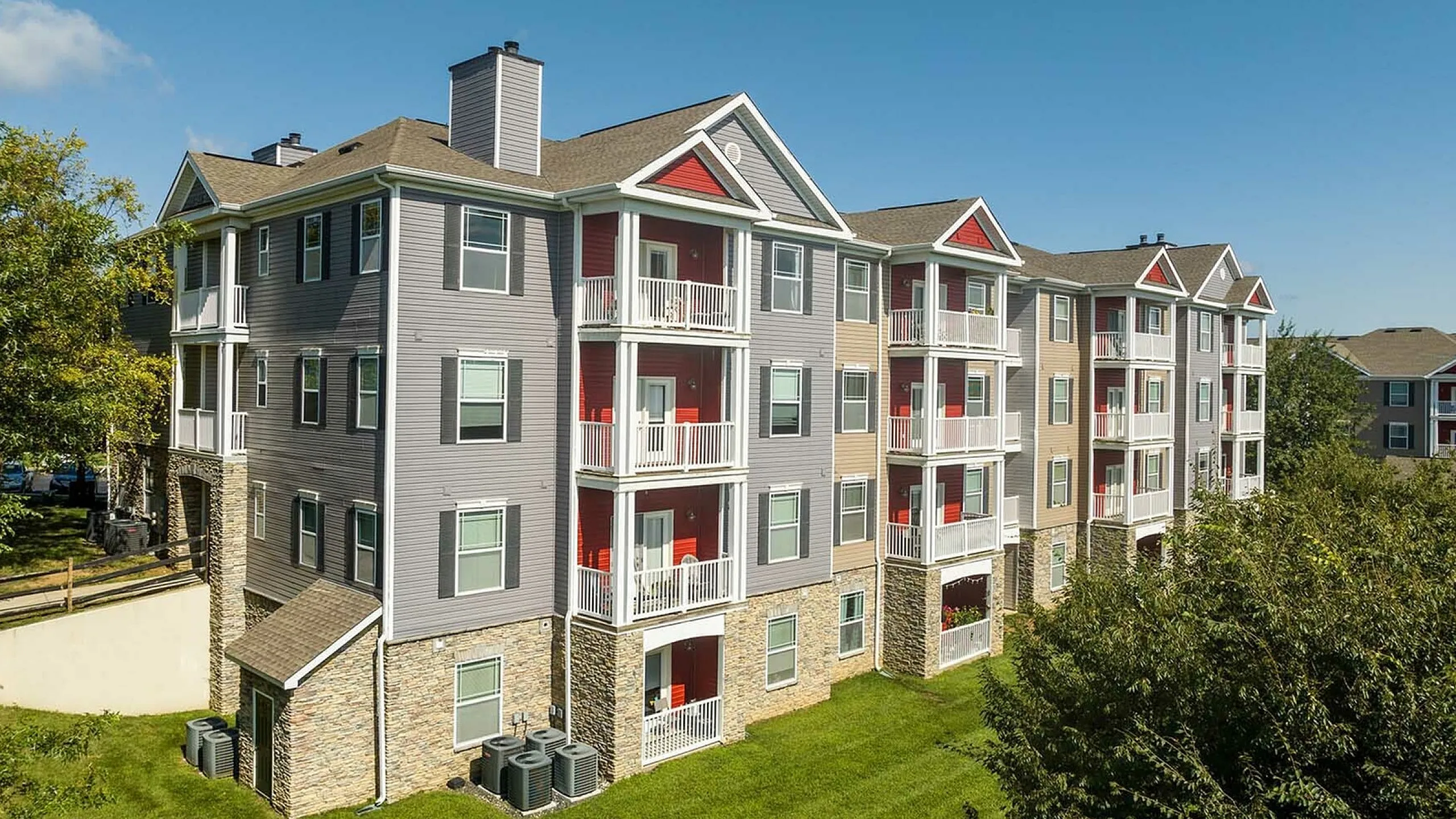 Charming multi-story apartment complex with modern design, private balconies, and lush green surroundings under a clear blue sky.