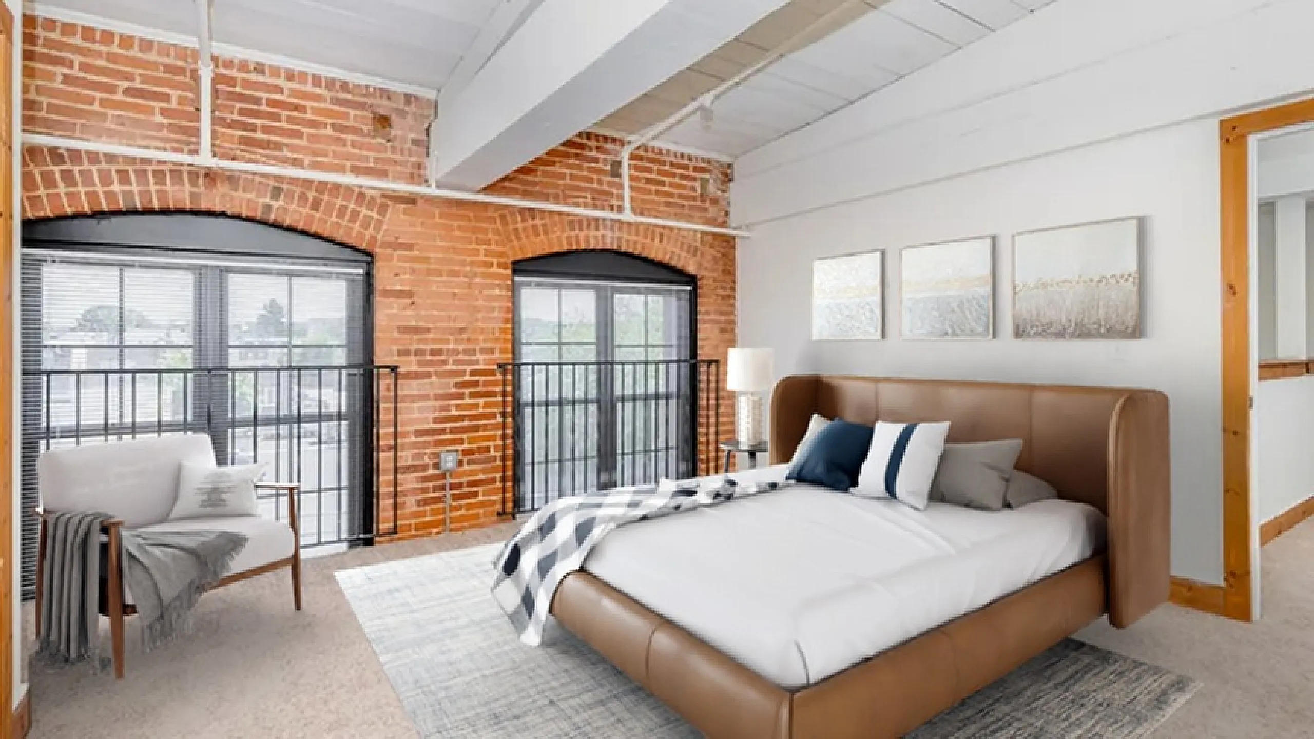 Chic bedroom featuring exposed brick walls, large windows with modern black frames, and a stylish brown leather bed offering a cozy retreat.