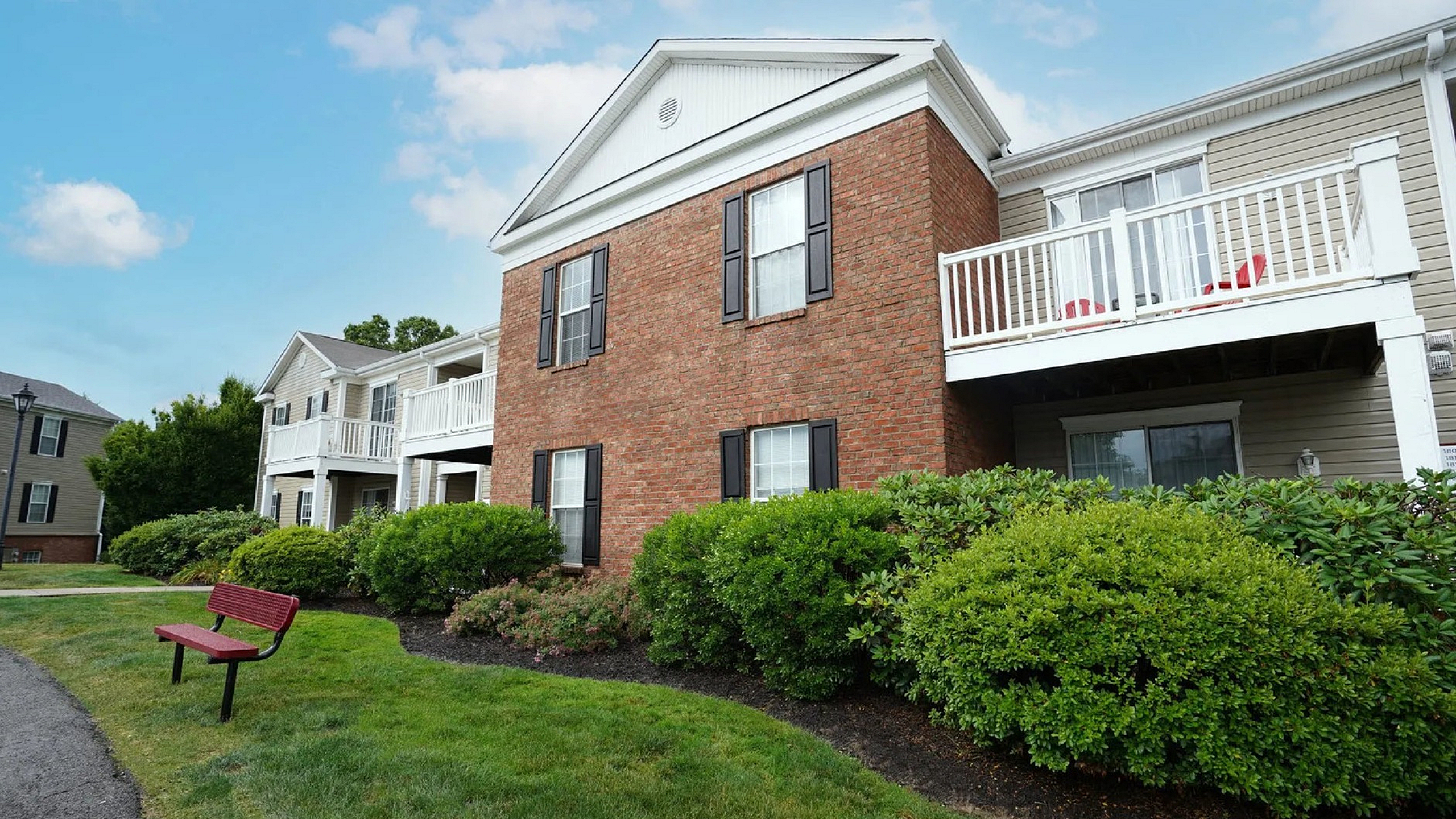 Charming apartment complex with a brick facade, lush landscaping, and inviting balconies under a bright blue sky.